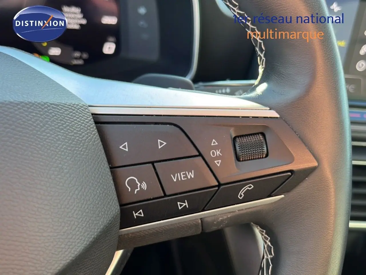 Gros plan sur les commandes au volant côté gauche d'une SEAT Leon gris magnétique, avec boutons multifonctions visibles.