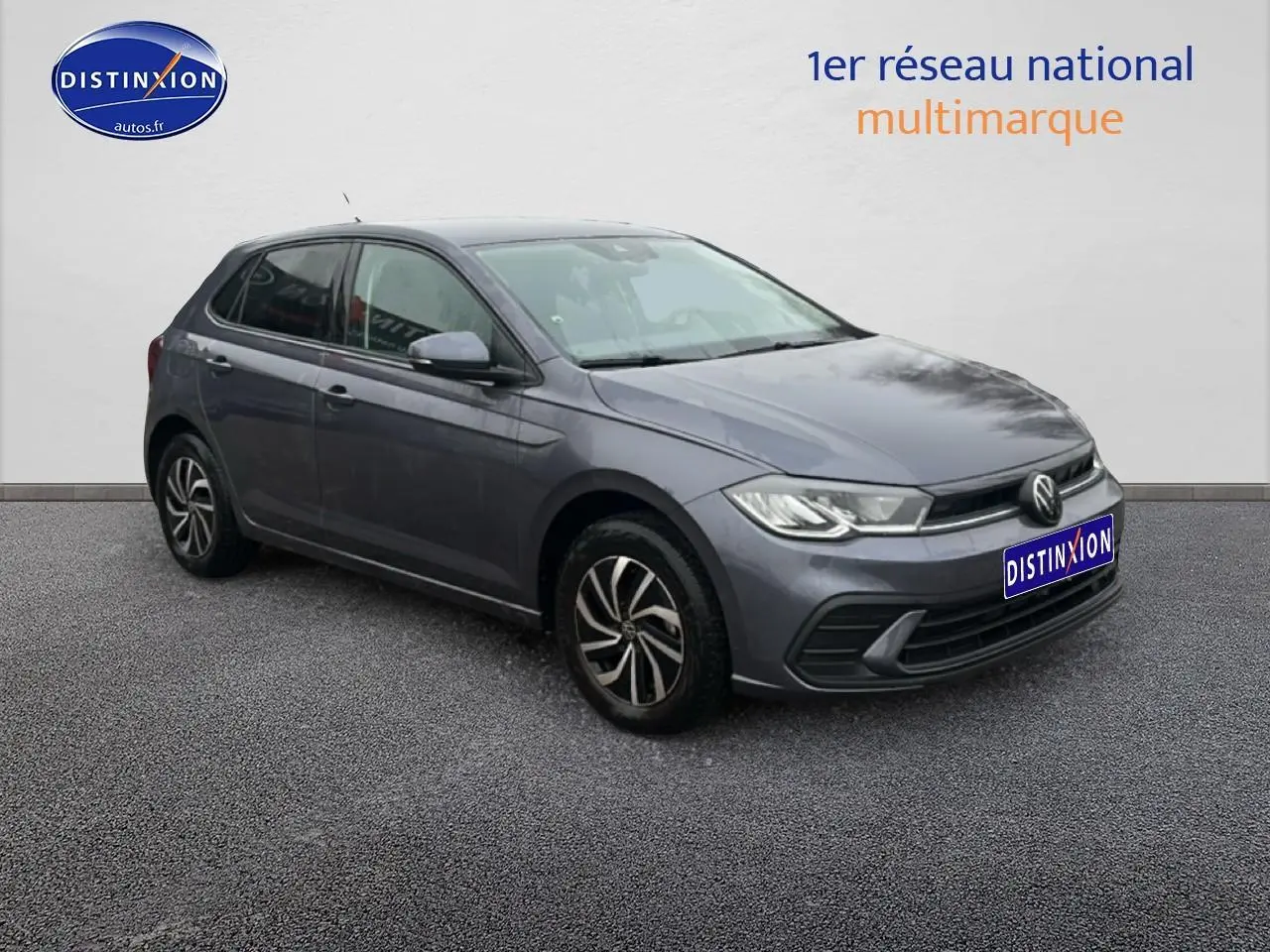 Volkswagen Polo gris cendre vue 3/4 avant droit sur sol gris avec calandre noire et jantes alliage.