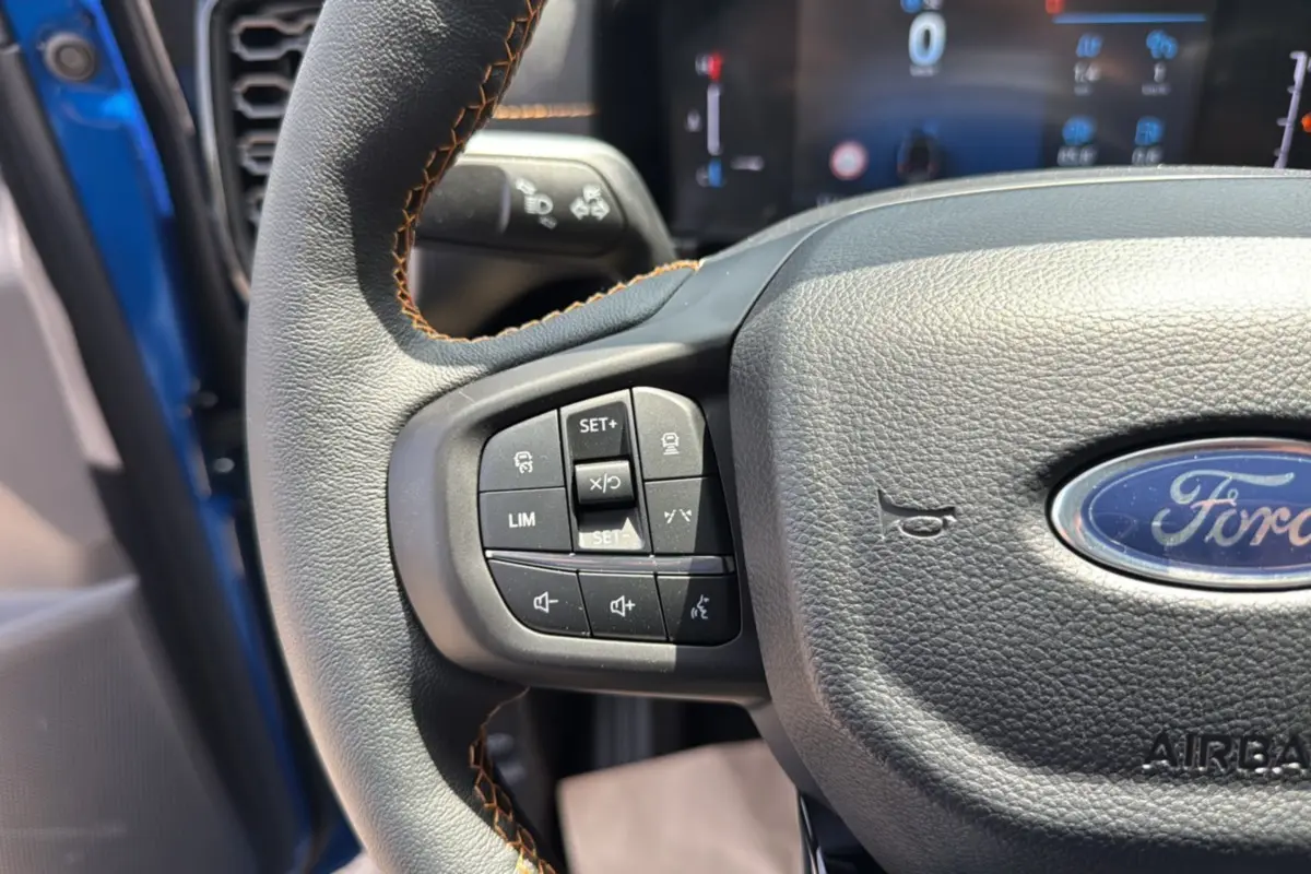 Gros plan sur le volant cuir multifonctions du Ford Ranger bleu lightning, avec commandes de régulateur et audio visibles.