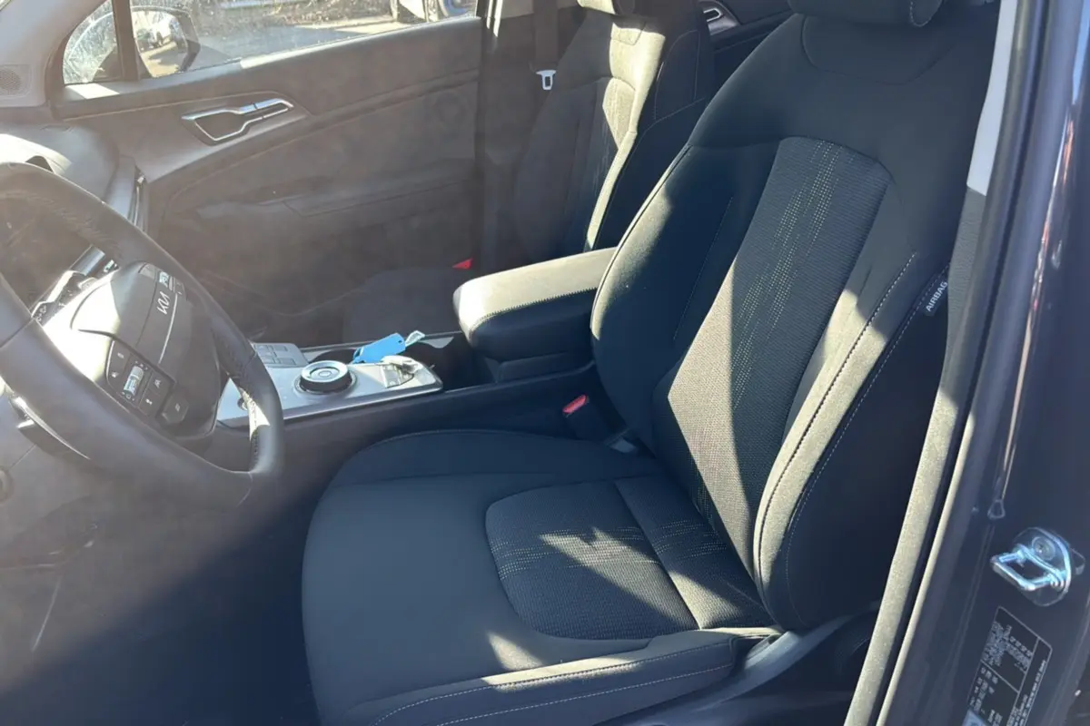 Intérieur avant du Kia Sportage gris eclipse 2026, vue côté droit sur siège tissu et console centrale avec volant cuir multifonctions.
