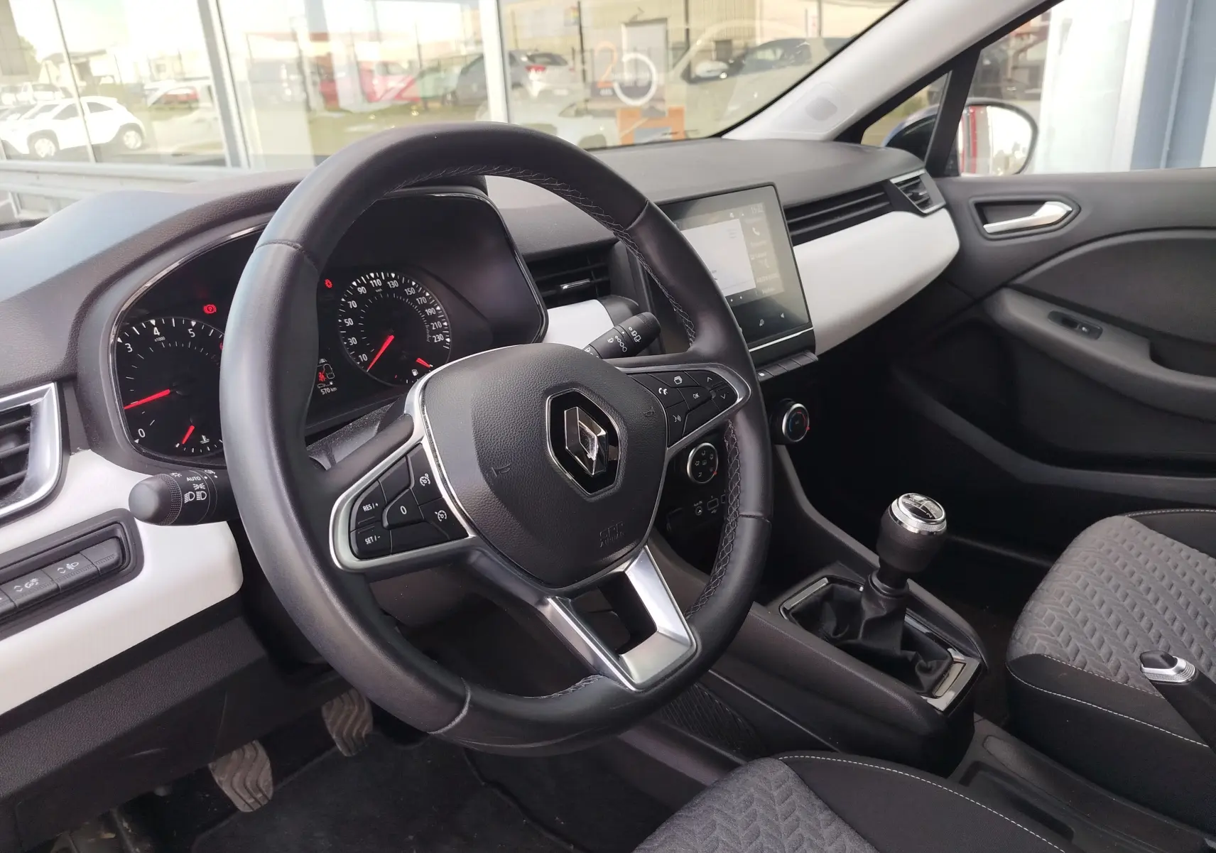 Vue intérieure côté conducteur de la Renault Clio 2022, volant multifonction, tableau de bord noir et blanc, boîte manuelle.