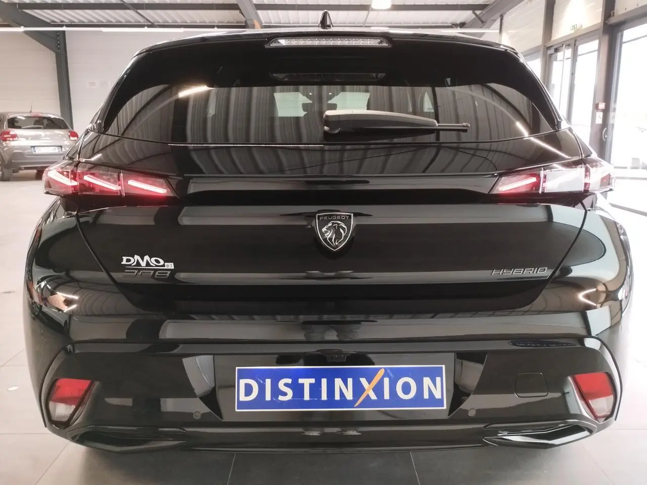 Vue arrière d'une Peugeot 308 hybride noire métallisée avec feux arrière LED en forme de griffes et logo central lumineux.
