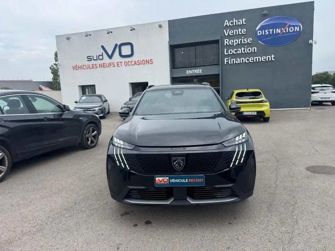 Vue avant d’un Peugeot 5008 Hybrid noir 2025 avec calandre distinctive et feux LED en griffes, stationné devant un concessionnaire.
