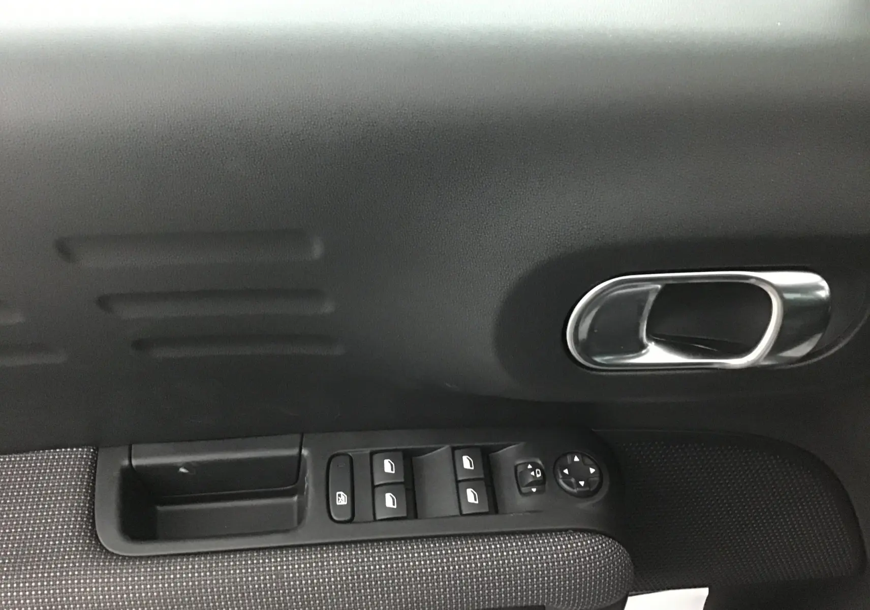 Gros plan sur la porte côté gauche de la Citroën C3 Aircross gris platinium, montrant les commandes des vitres et la poignée chrome.