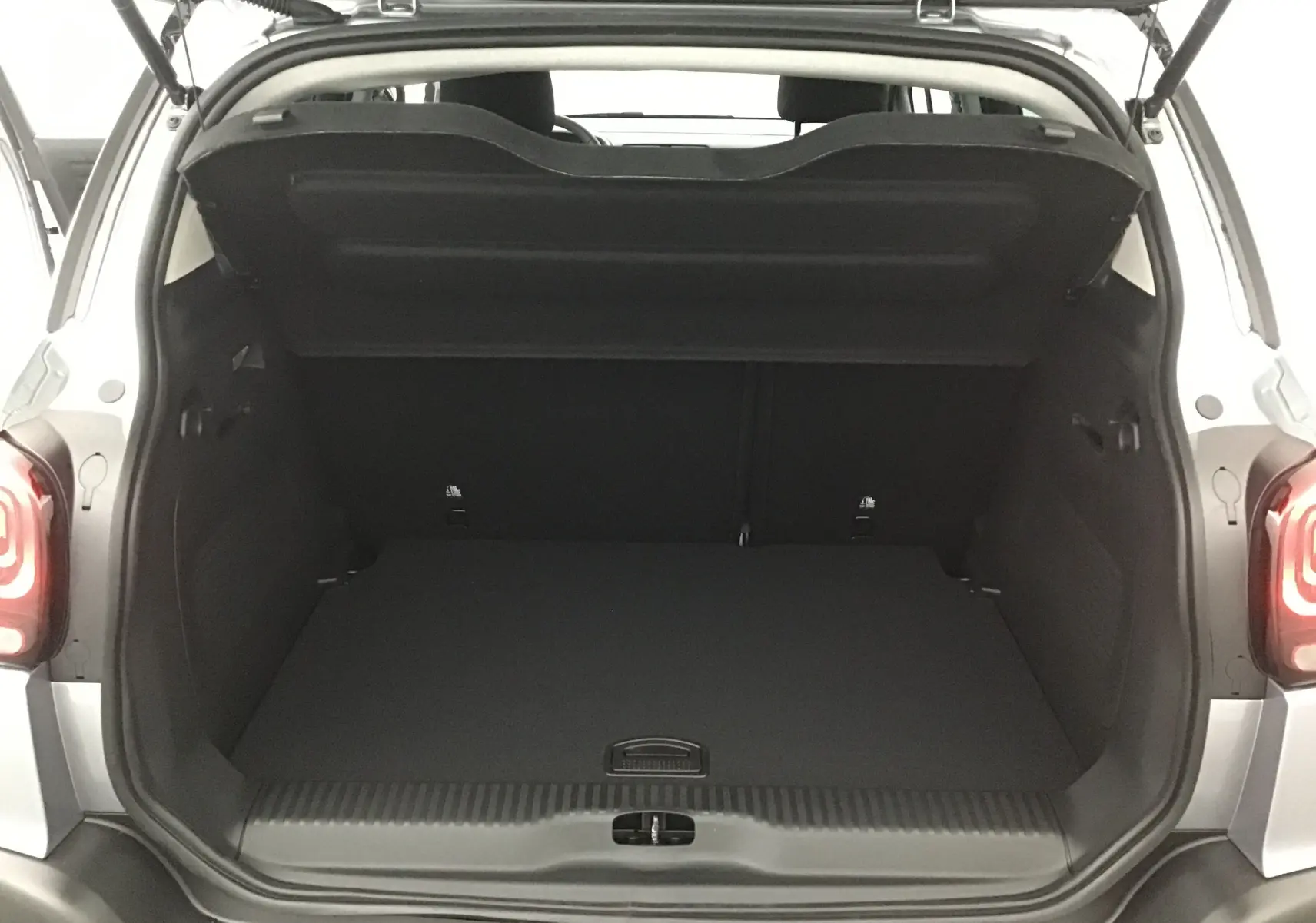 Coffre ouvert vu de l'arrière d'un Citroën C3 Aircross gris platinium avec intérieur noir et feux arrière allumés.
