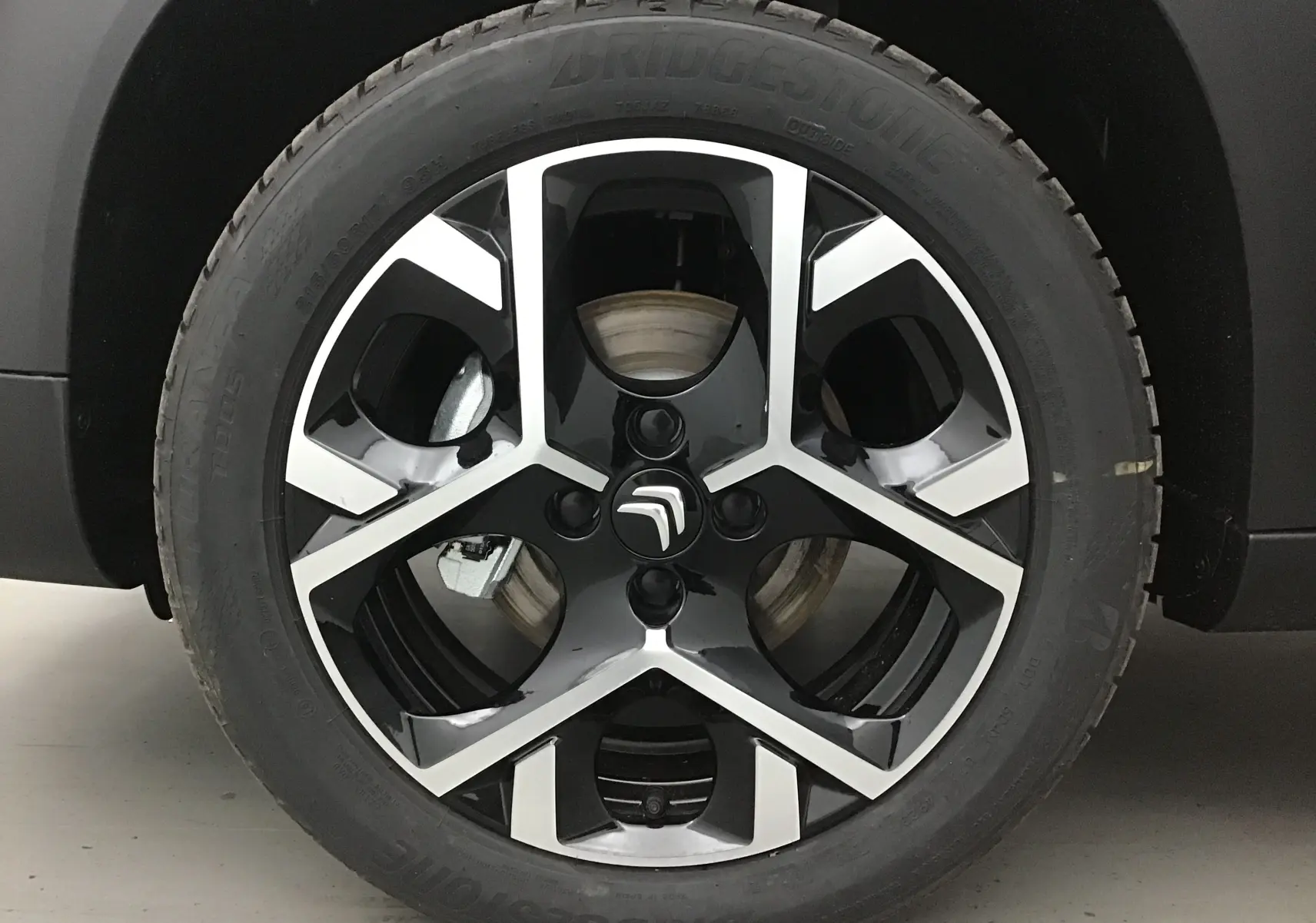 Gros plan sur la jante alliage noire et argentée avec logo Citroën du côté gauche d’un C3 Aircross gris platinium.