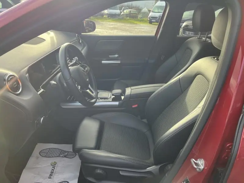 Vue intérieure côté conducteur du Mercedes GLA 200 rouge Patagonie, sièges en tissu/similicuir noir et tableau de bord moderne.