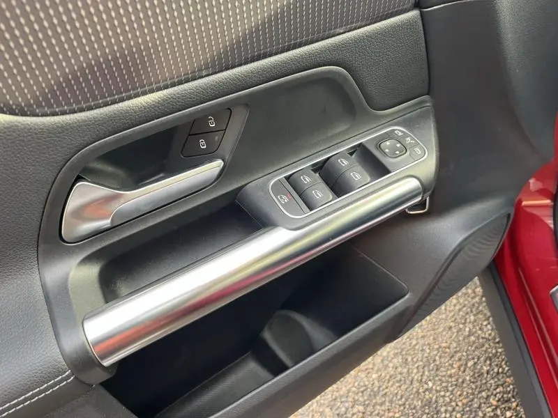 Gros plan sur la porte côté gauche du Mercedes GLA rouge Patagonie, avec commandes de vitres et poignée alu.