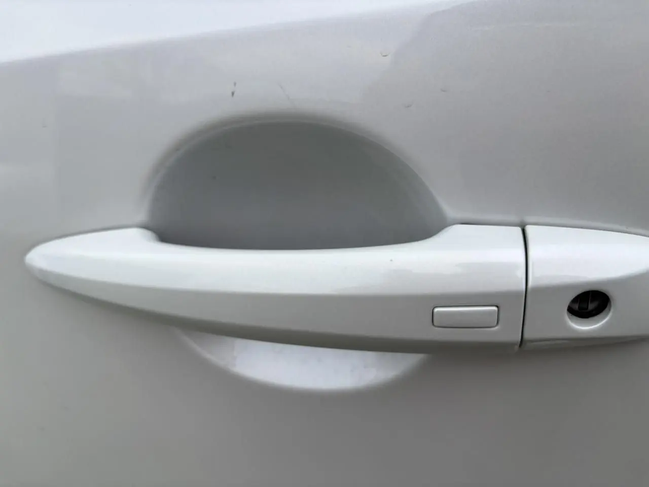 Poignée de porte blanche nacrée du Nissan Qashqai III 2025 vue de près, avec bouton de déverrouillage intégré.