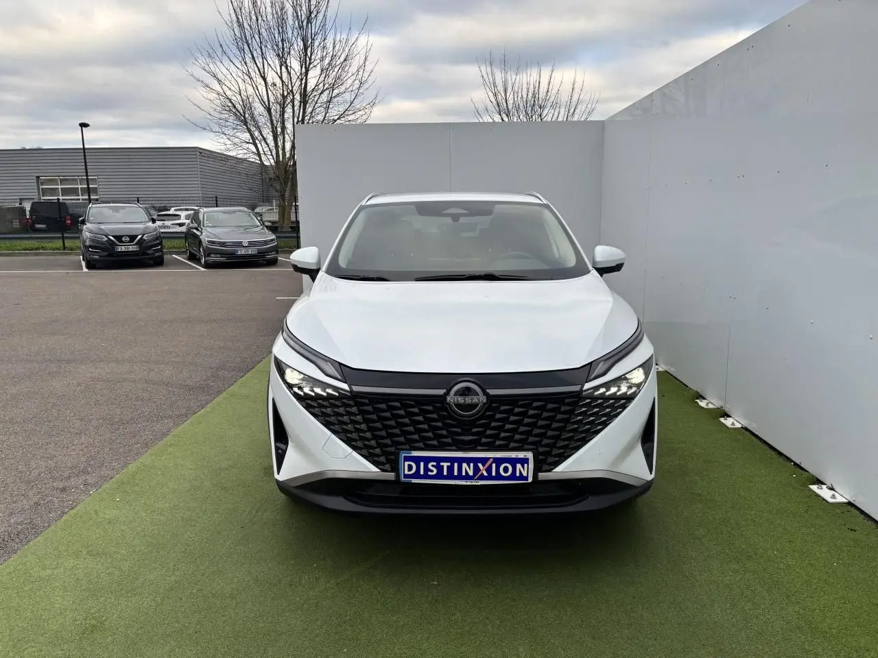 Vue de face du Nissan Qashqai blanc nacré avec calandre noire texturée et phares LED allumés.
