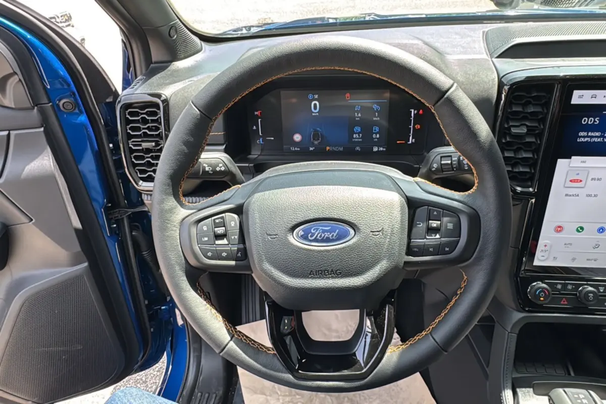 Vue intérieure centrée sur le volant cuir noir avec surpiqûres orange du Ford Ranger Bleu Lightning 2025.