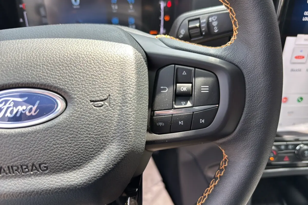 Gros plan sur le volant cuir noir avec surpiqûres orange du Ford Ranger 205 Wildtrak X, boutons multifonctions visibles.