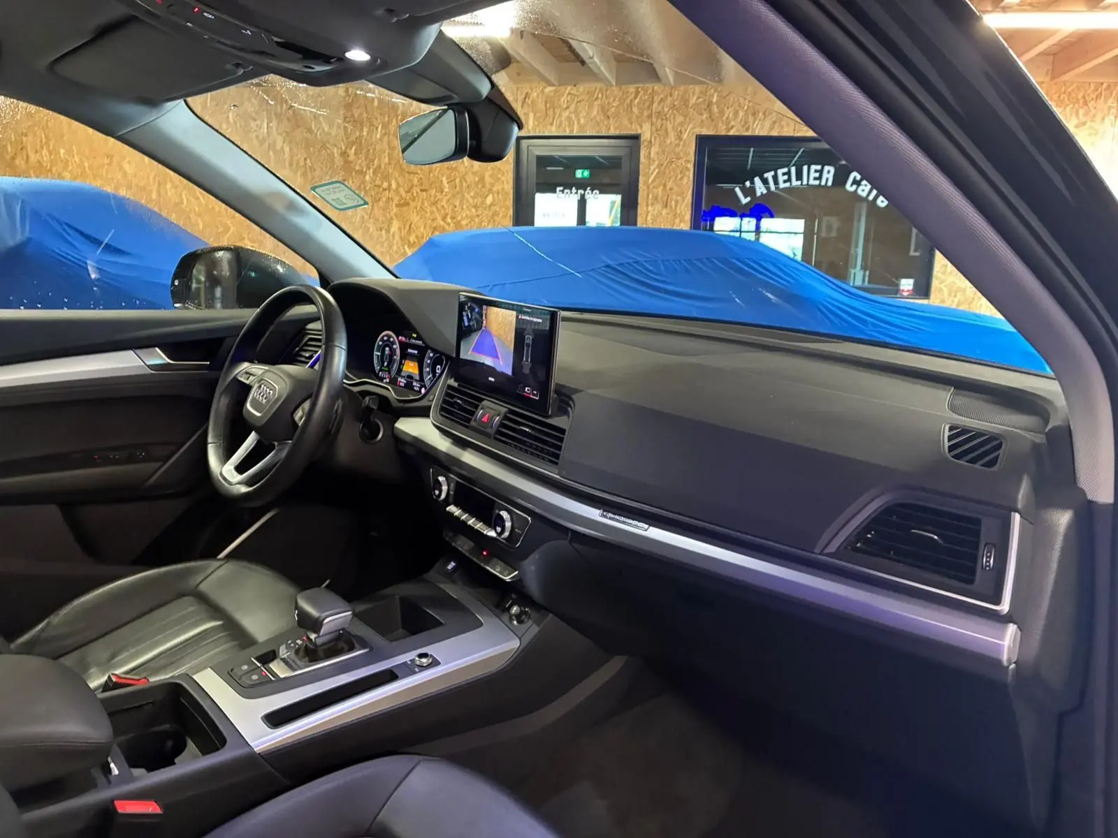 Intérieur de l'Audi Q5 2024 vu côté conducteur, tableau de bord noir avec écran central et volant cuir multifonction.