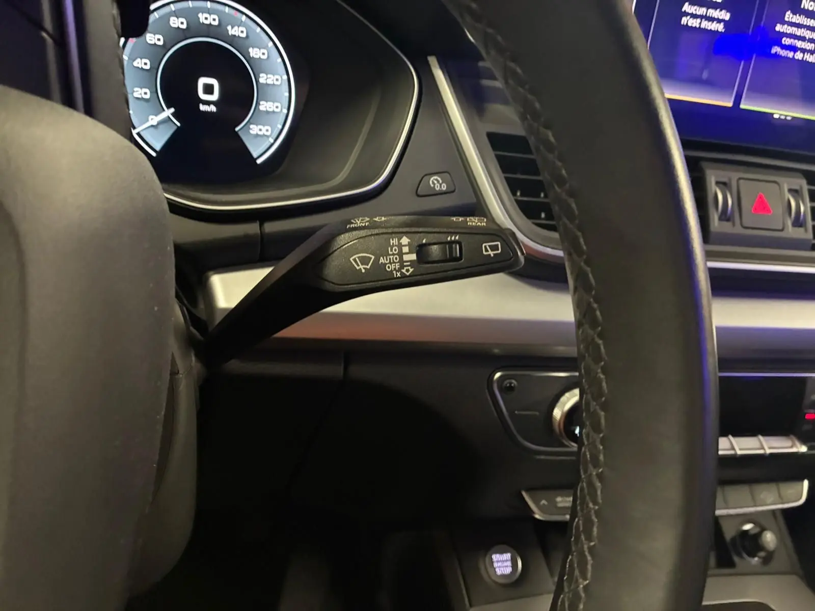 Gros plan sur le commodo de lève-glace à gauche du volant cuir d’un Audi Q5 gris hybride rechargeable 2024.