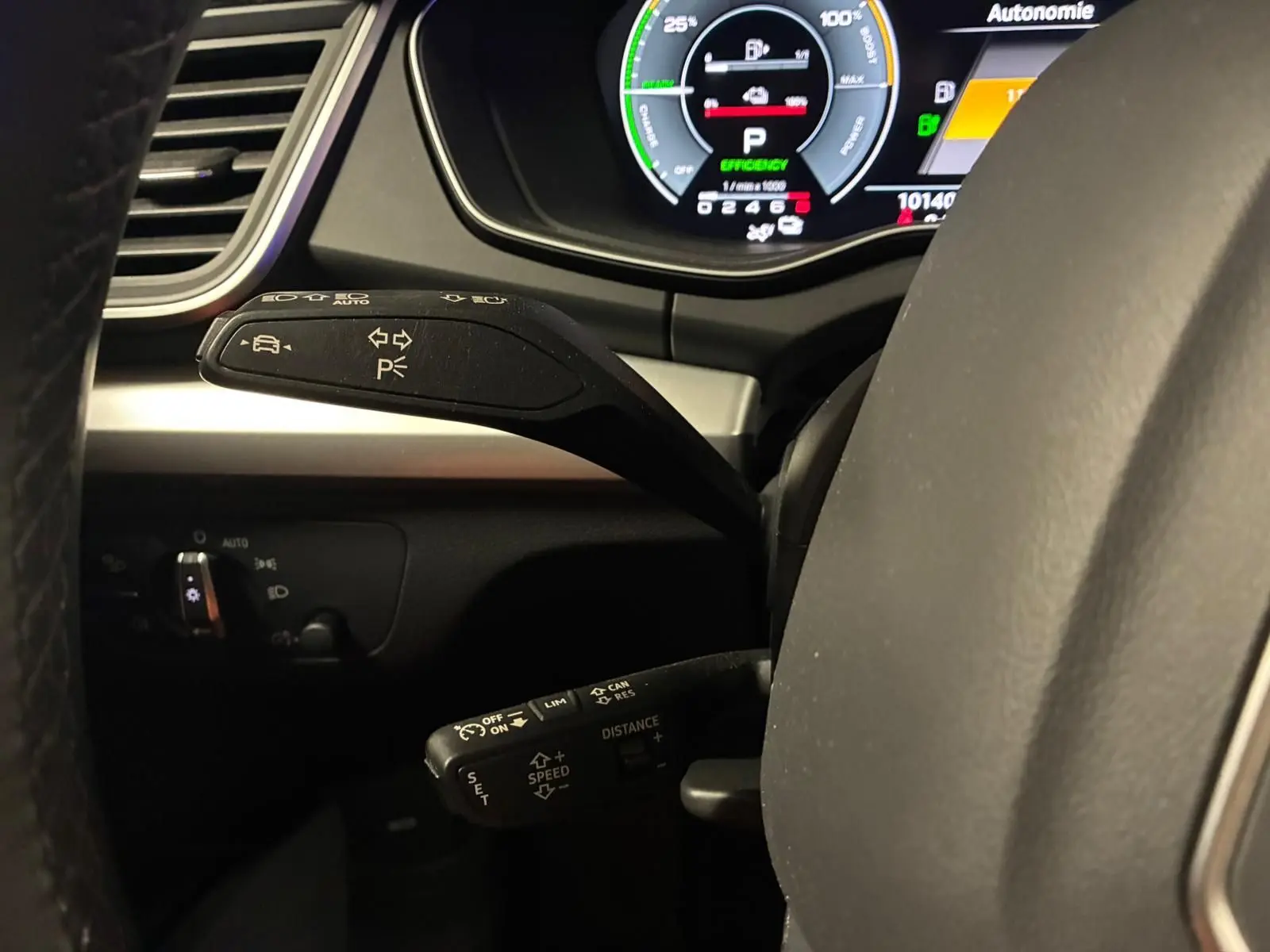 Gros plan sur les commandes au volant côté gauche de l'Audi Q5 gris, avec tableau de bord numérique en arrière-plan.