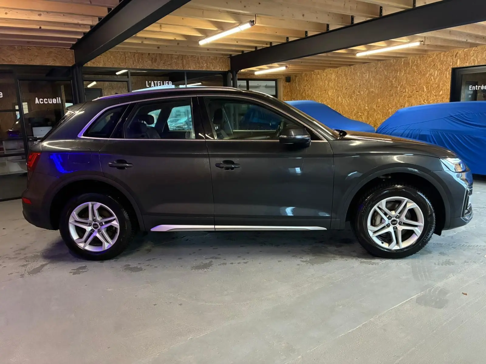 Audi Q5 gris vue de profil côté gauche dans un garage, avec jantes 5 branches doubles et moulures argentées.