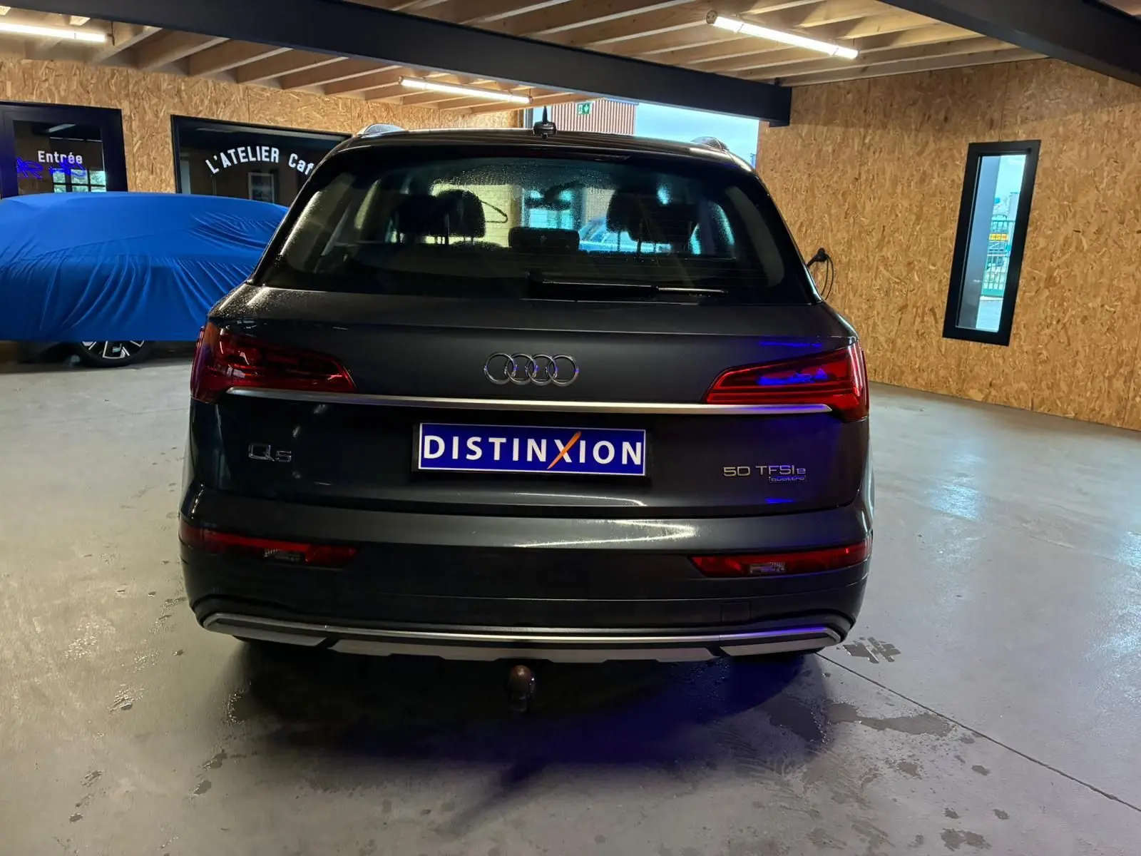 Vue arrière d'un Audi Q5 gris 2024 hybride rechargeable avec attelage visible en intérieur d'atelier.