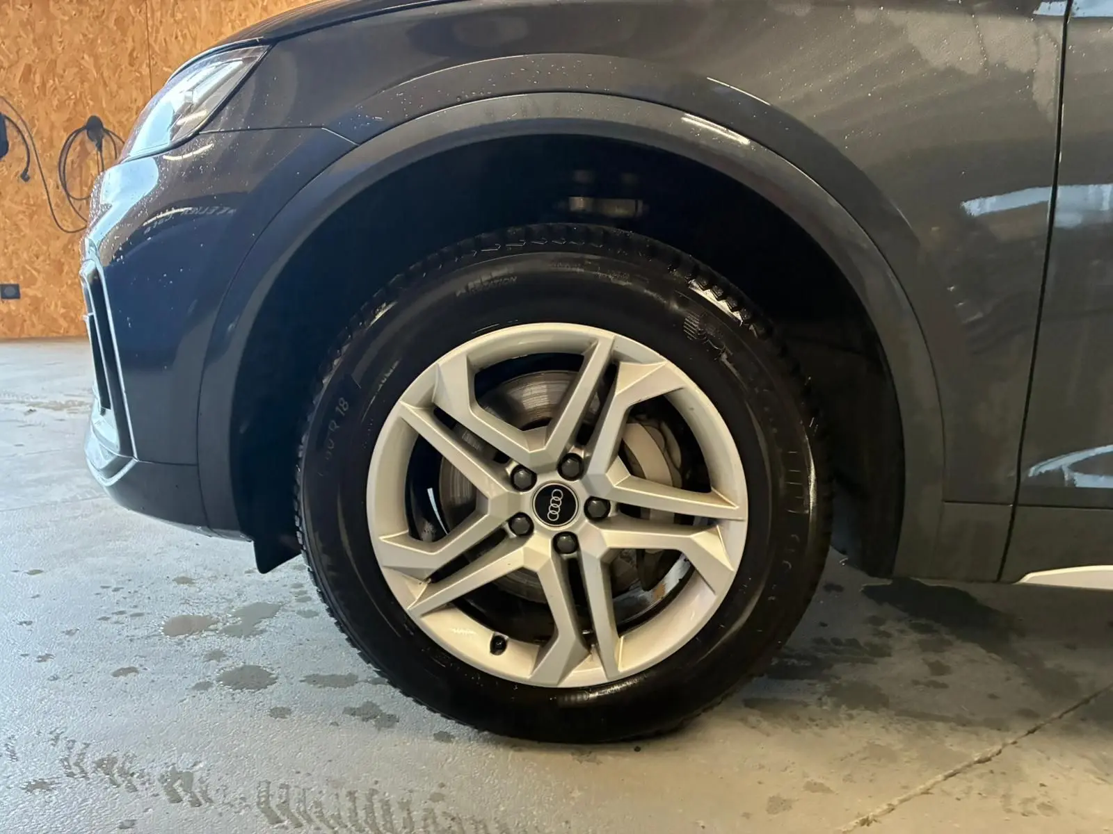 Vue de côté droit avant sur l’Audi Q5 gris avec passage de roue noir grainé et partie avant visible en intérieur.