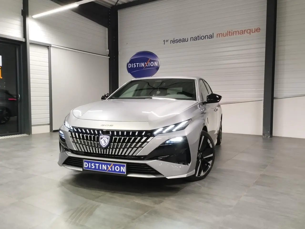 PEUGEOT 308 gris Artense vue 3/4 avant en intérieur, avec calandre lumineuse et jantes noires.