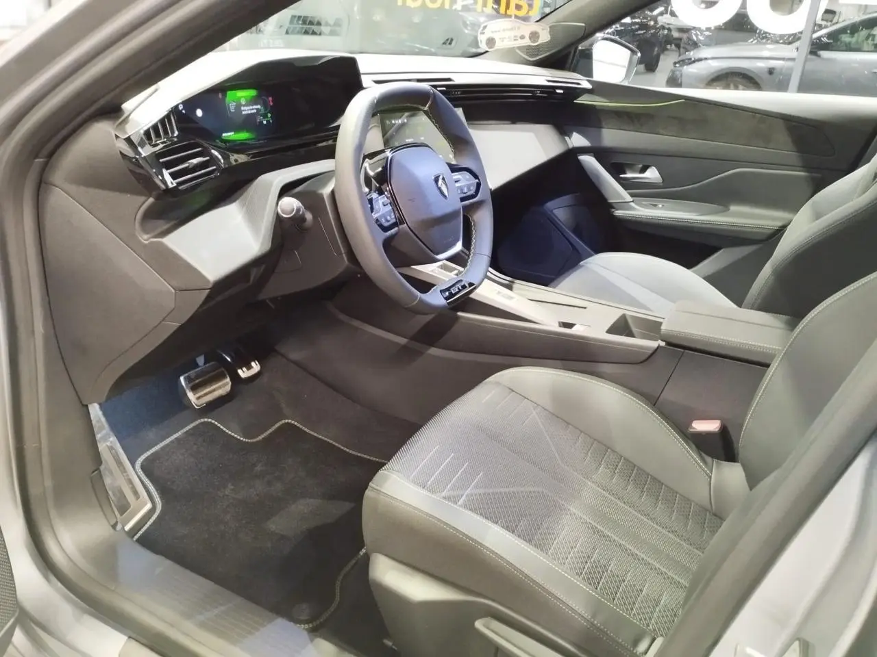 Vue intérieure côté conducteur de la Peugeot 308 gris Artense, avec volant compact GT et tableau de bord numérique 3D.