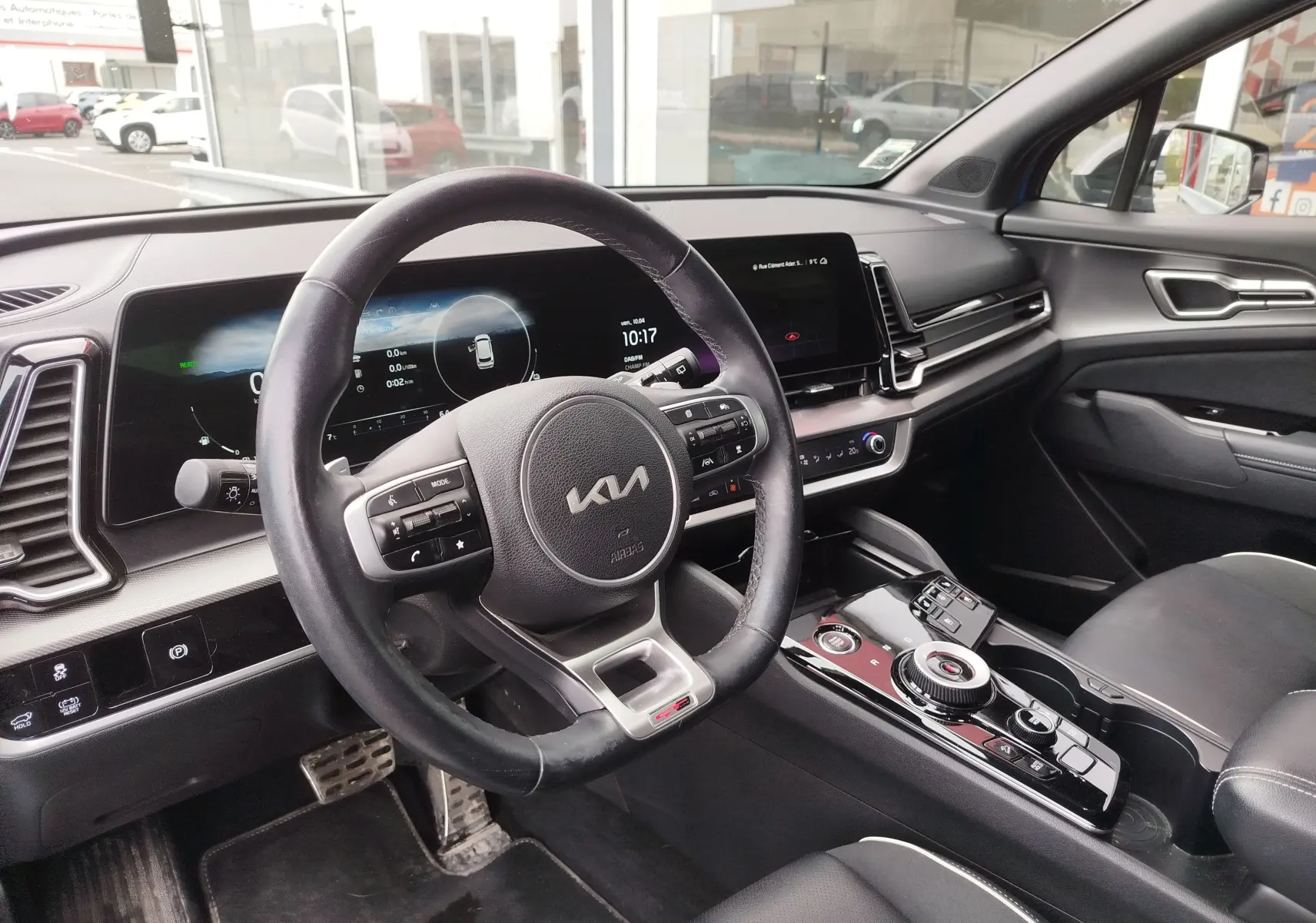 Vue intérieure côté conducteur du Kia Sportage 2022, volant cuir noir et tableau de bord digital moderne.