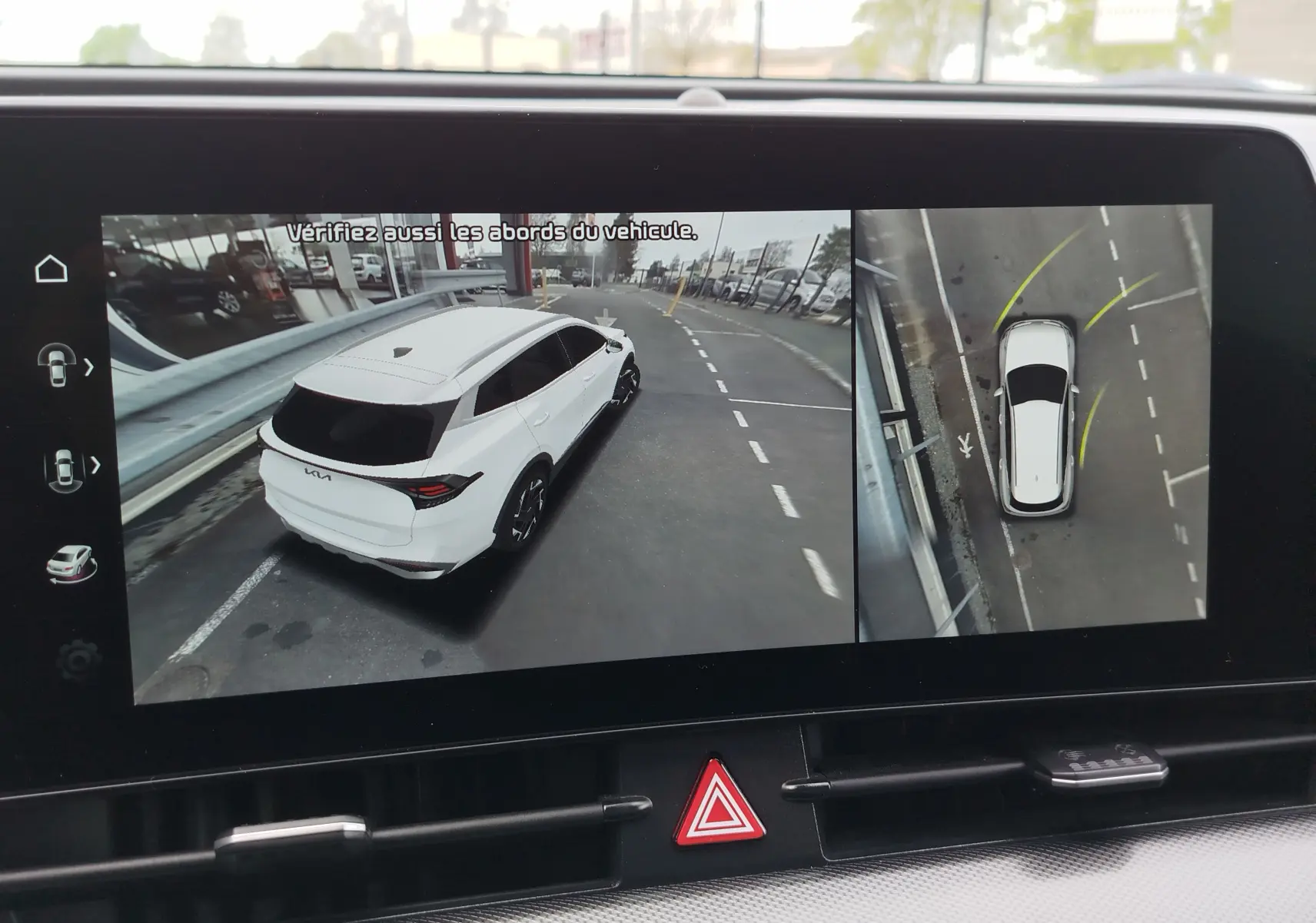 Affichage écran multimédia montrant une Kia Sportage blanche en vue 3/4 arrière et vue aérienne pour assistance au stationnement.