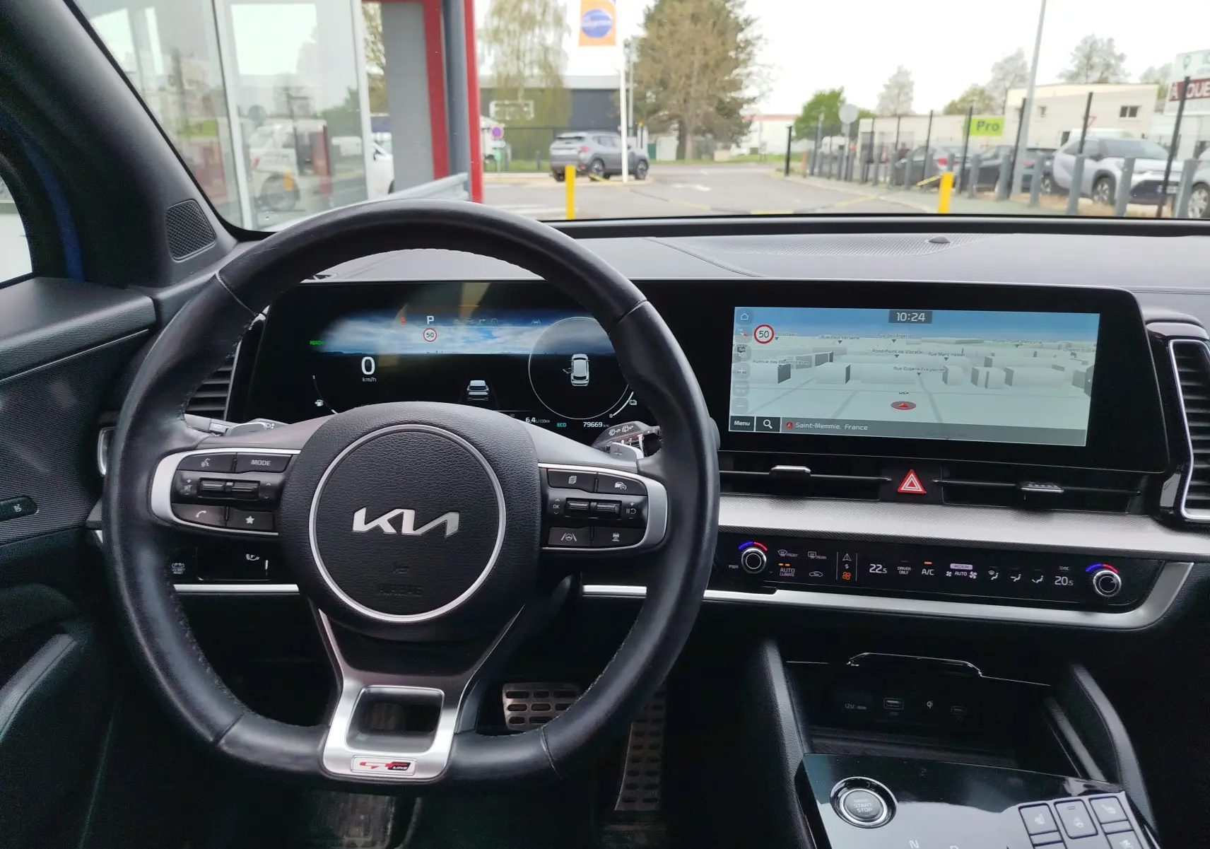 Vue intérieure centrée sur le volant et le tableau de bord numérique du Kia Sportage bleu, avec écran tactile de navigation.