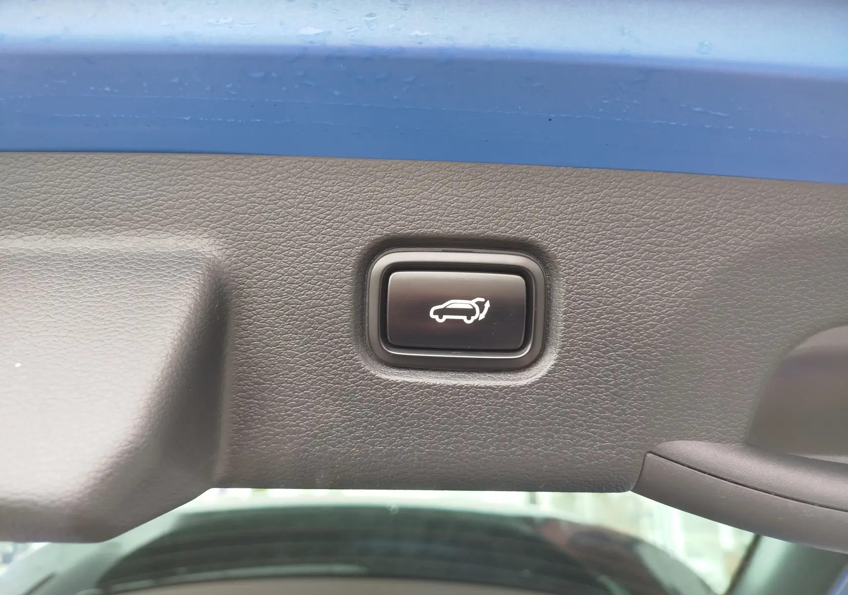 Bouton de fermeture électrique du hayon sur la partie intérieure du coffre d'un KIA Sportage bleu métallisé.