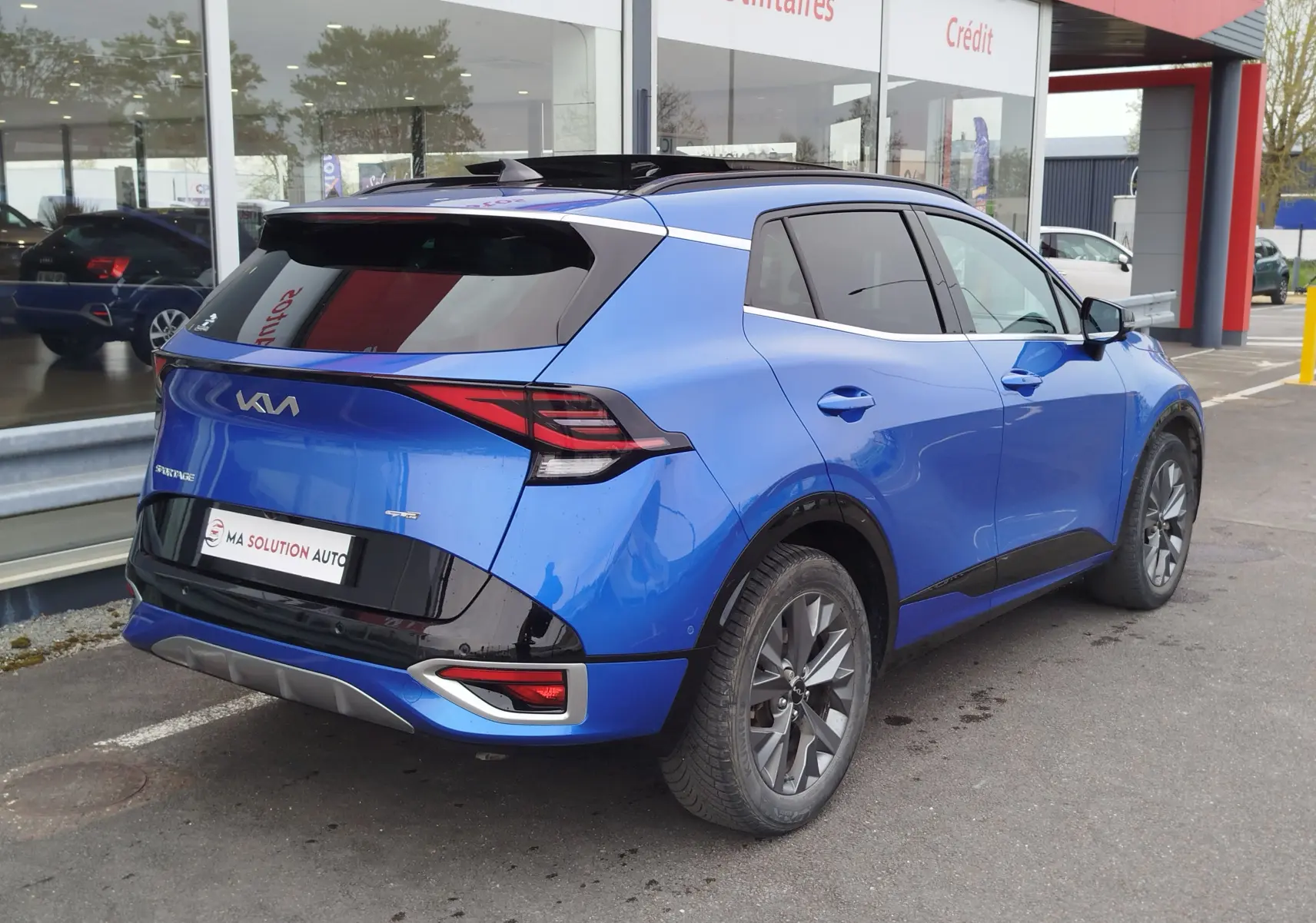 Vue 3/4 arrière droite du KIA SPORTAGE bleu métallisé avec toit noir et feux arrière LED distinctifs.