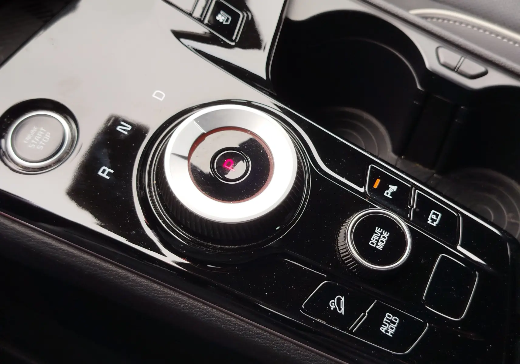 Gros plan sur la console centrale noire brillante du Kia Sportage 2022, avec sélecteur rotatif de boîte auto et boutons de contrôle.