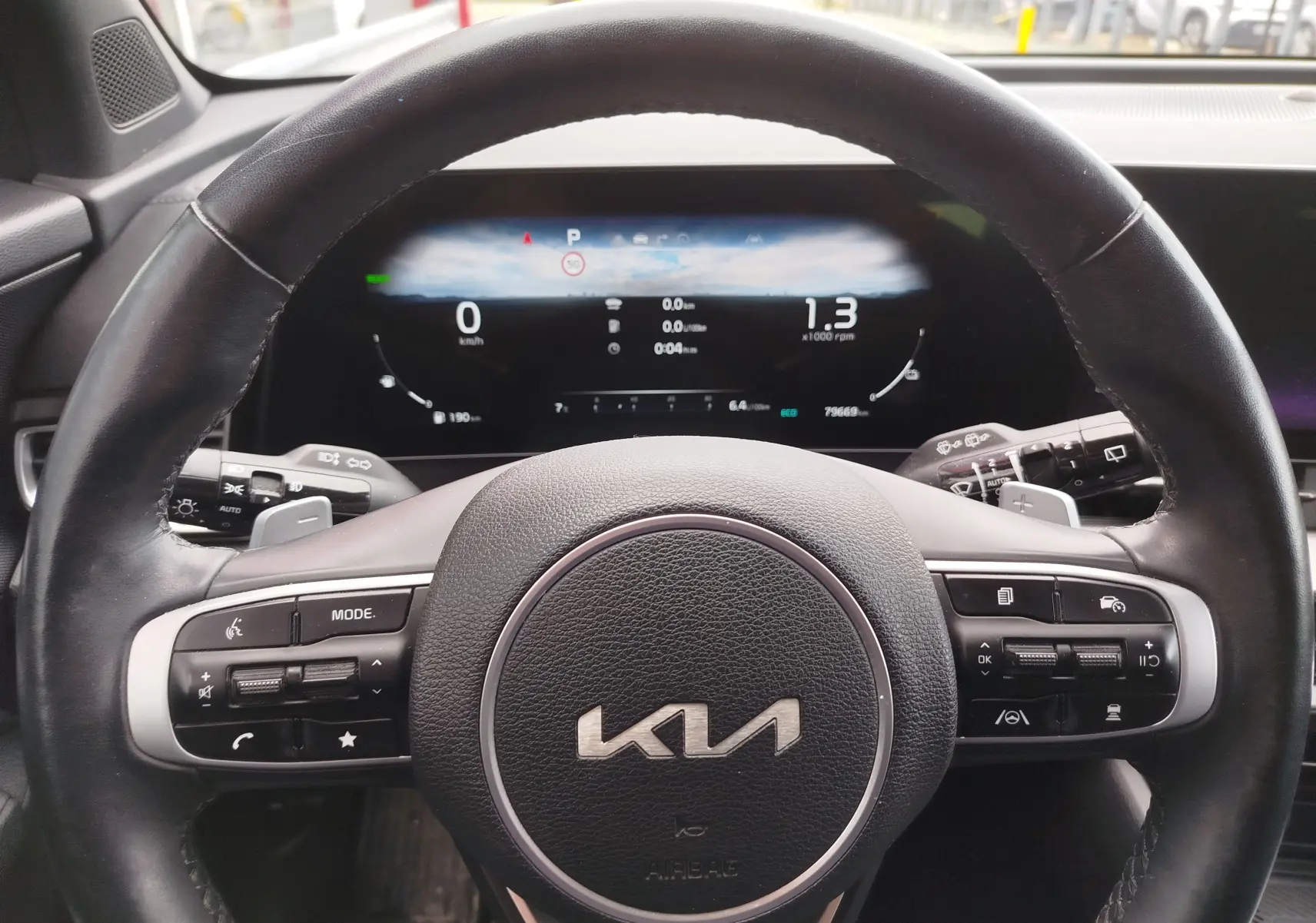 Vue rapprochée du volant noir du Kia Sportage 2022 avec tableau de bord numérique allumé en arrière-plan.