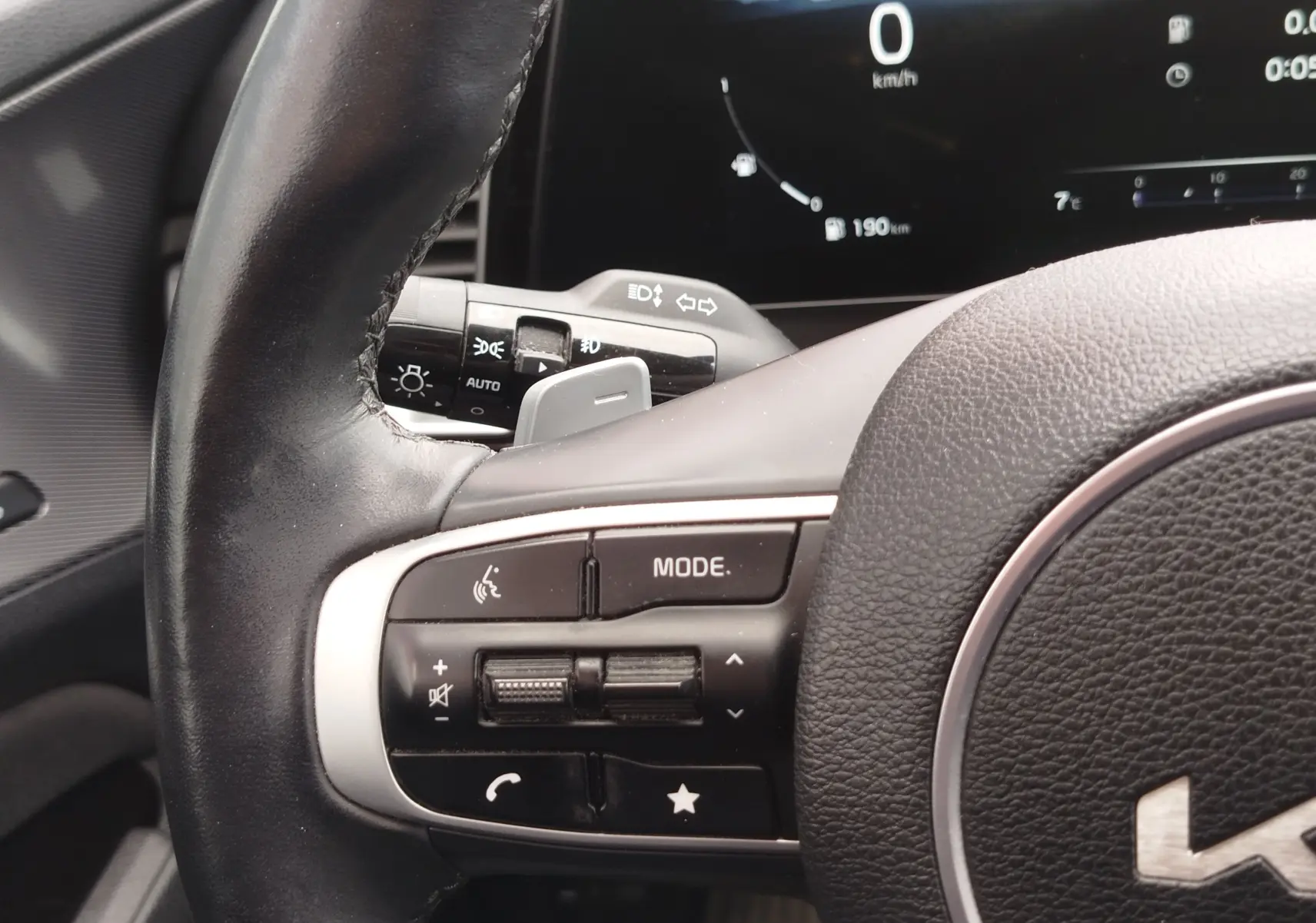 Gros plan sur le volant cuir noir côté gauche du Kia Sportage 2022 avec commandes multimédia et tableau de bord numérique.