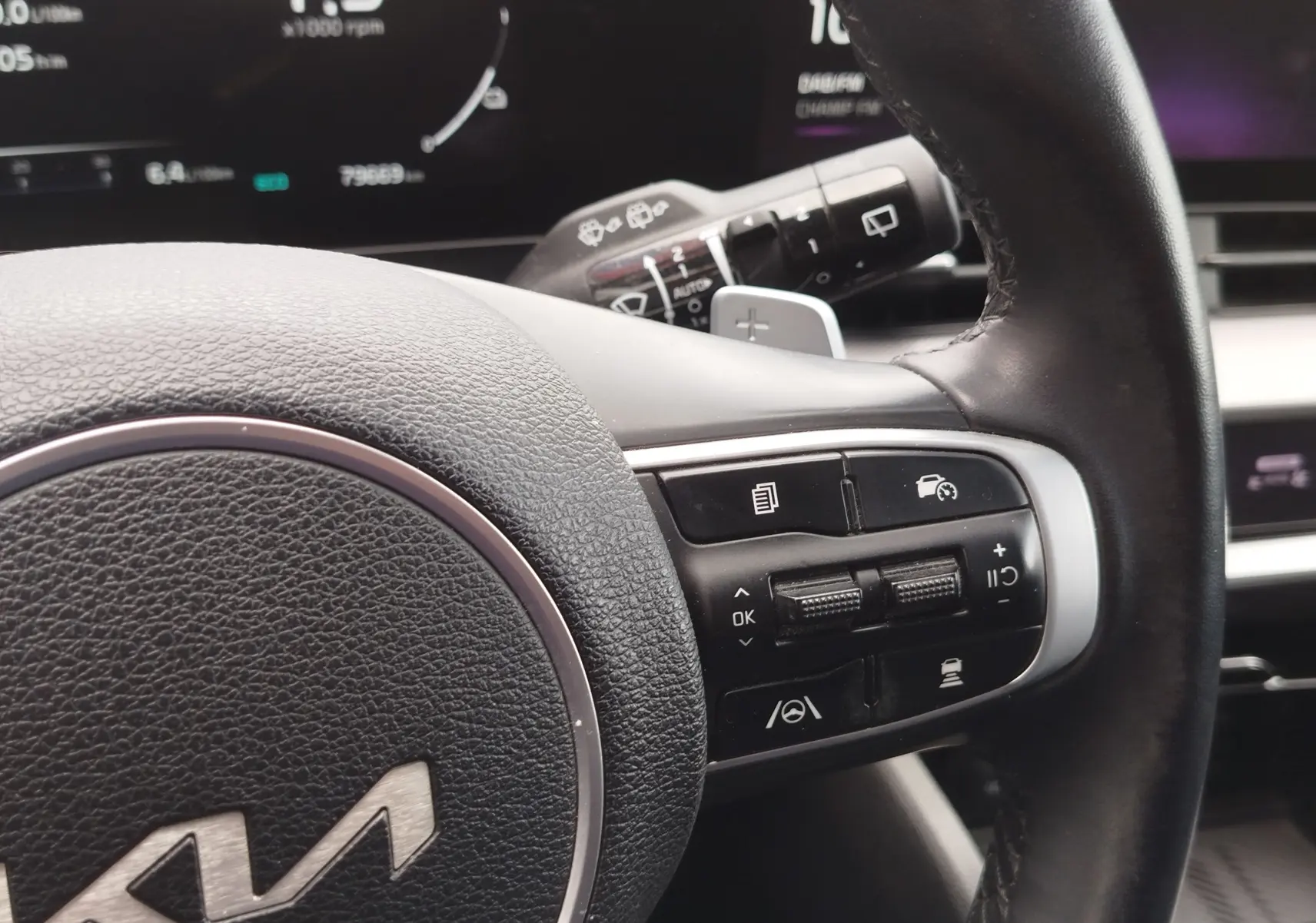 Gros plan sur les commandes au volant en cuir noir du Kia Sportage 2022, affichage numérique en arrière-plan.