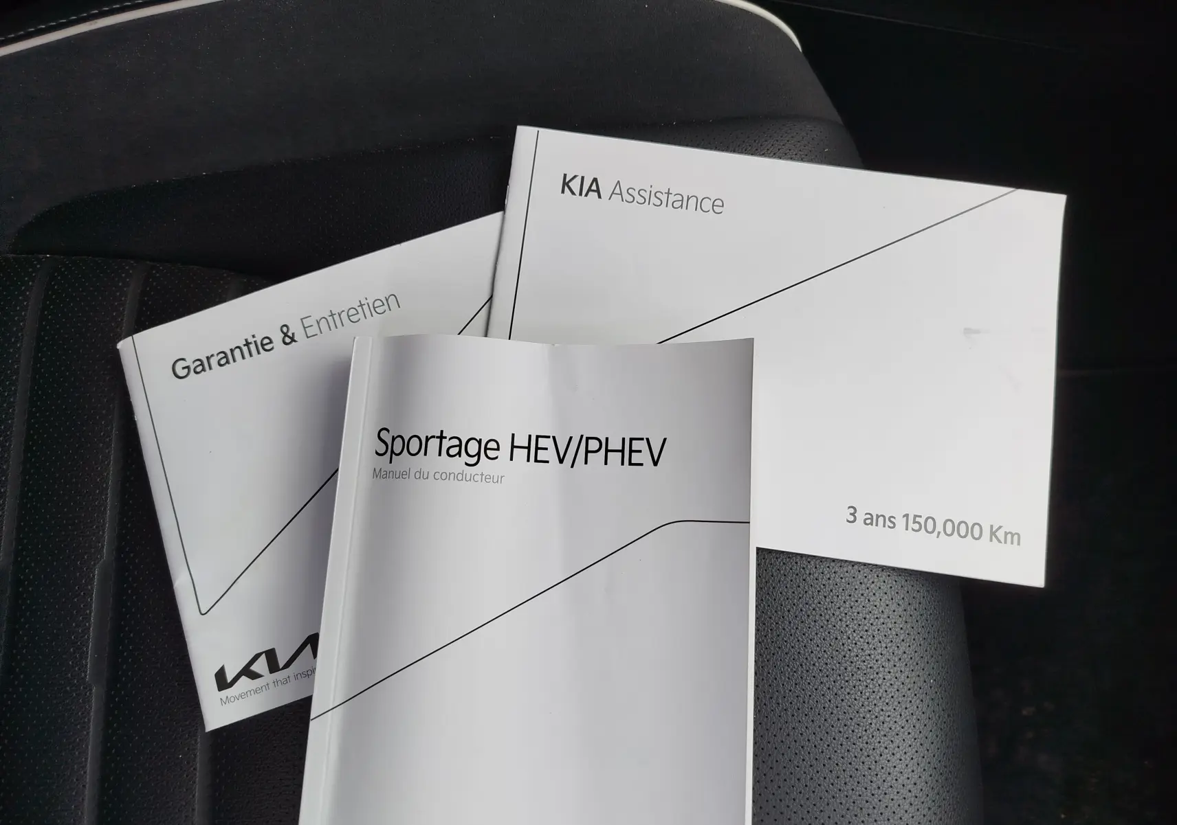 Manuels KIA Sportage HEV/PHEV posés sur un siège en cuir noir, sans vue du véhicule.