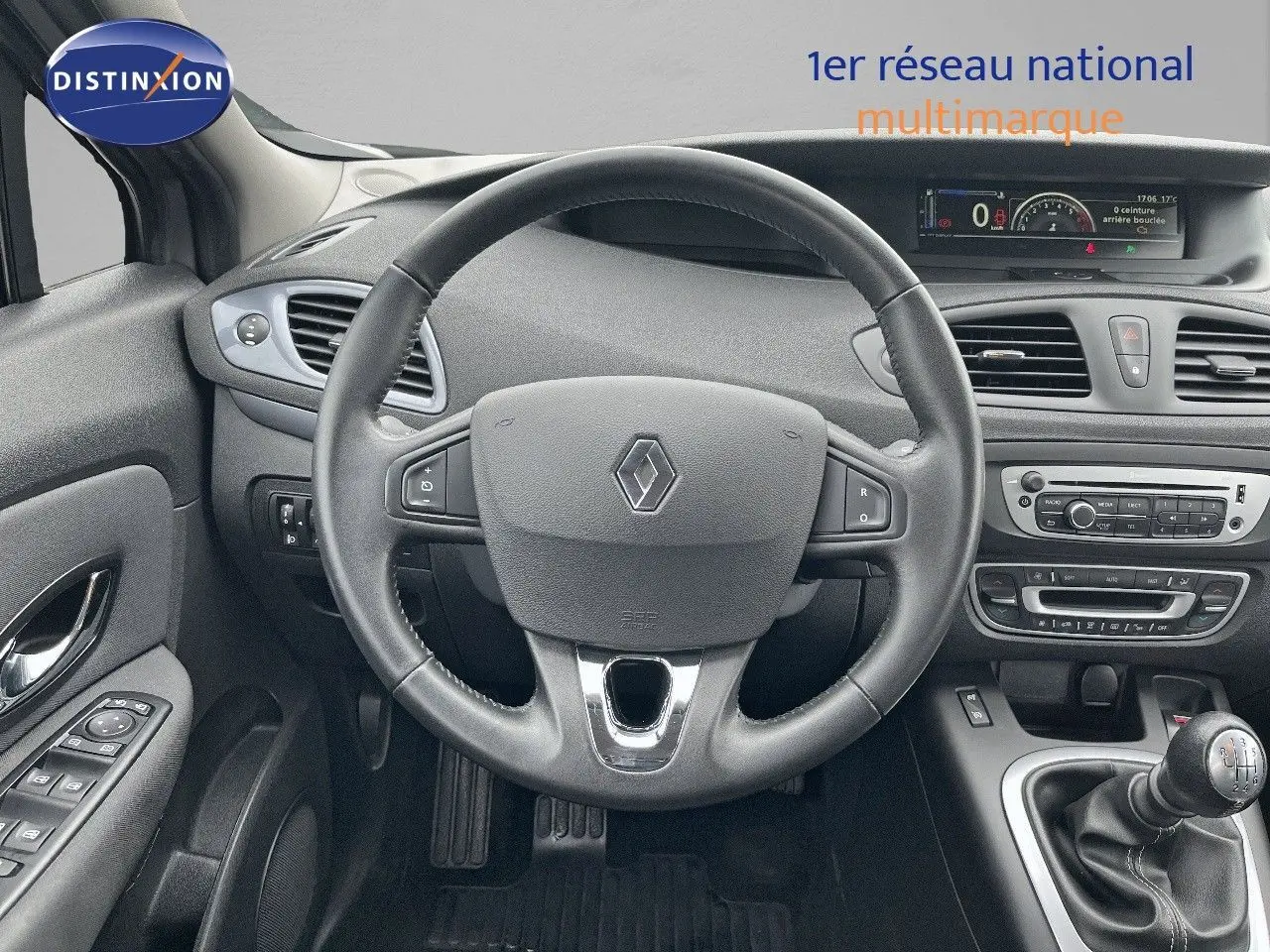 Vue intérieure frontale du tableau de bord gris du Renault Scénic III 2015 avec volant et levier de vitesse manuel.