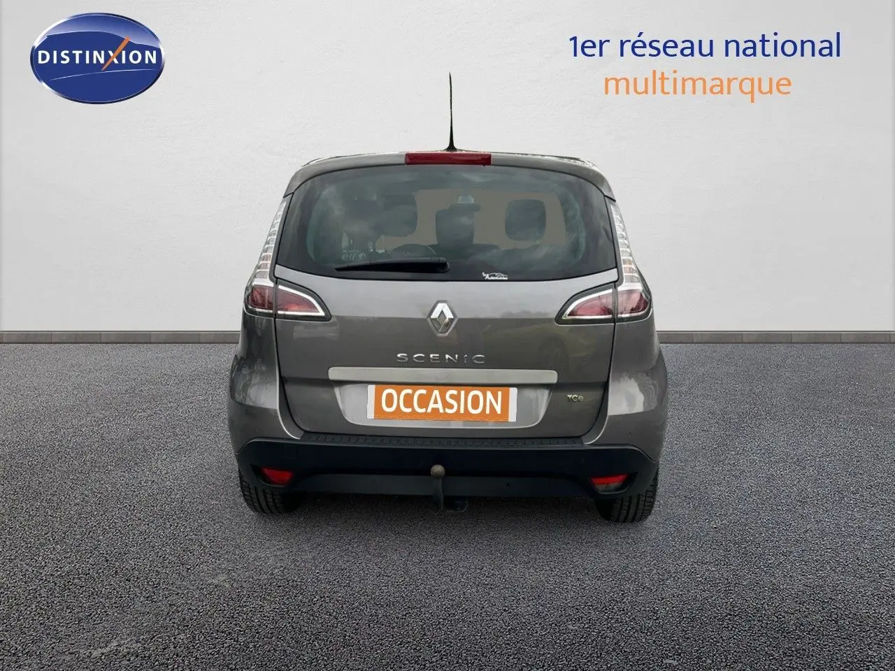 Vue arrière d’un Renault Scénic III gris 2015 avec attelage et plaque « occasion » visible.
