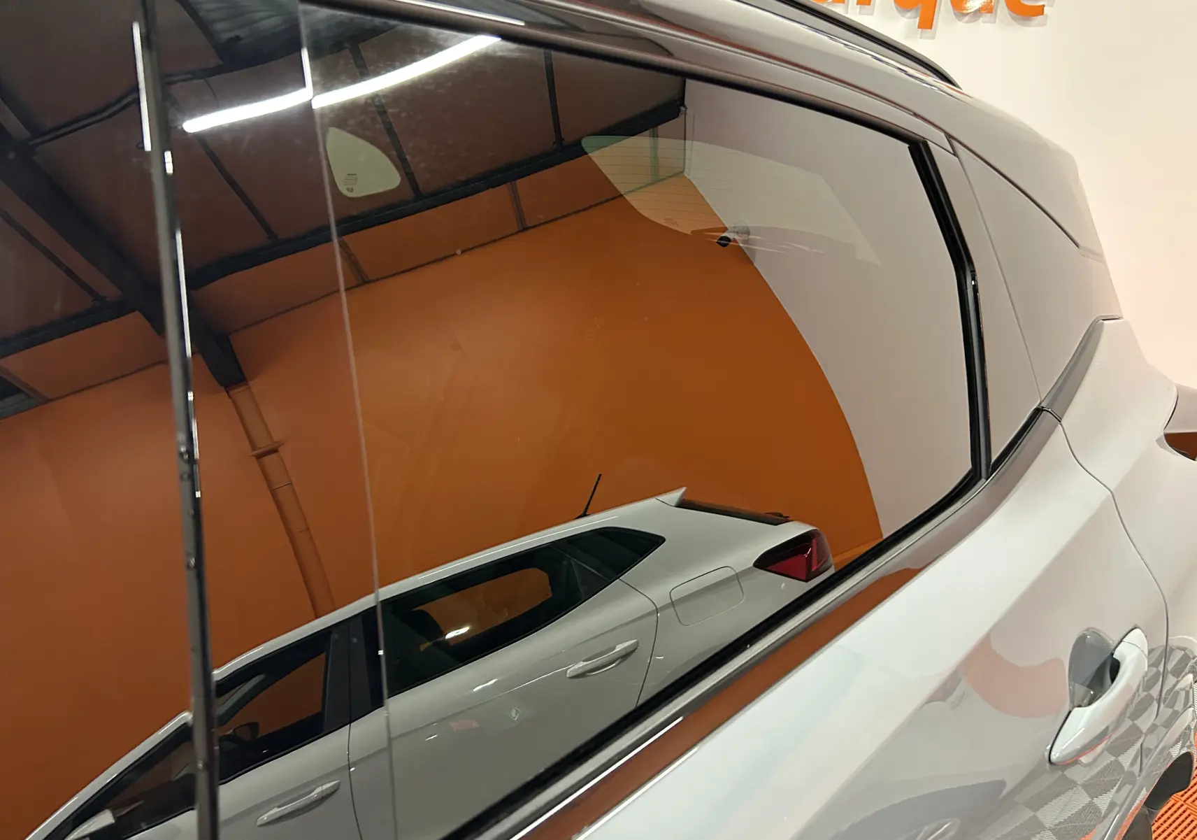 Reflet latéral droit du Nissan Qashqai 2025 gris céramique métal avec toit noir dans un intérieur orange.