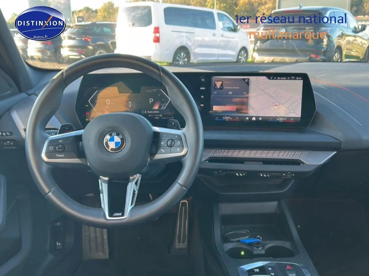 Vue intérieure centrée sur le volant BMW et l'écran tactile du tableau de bord d'une Série 1 blanche alpin.