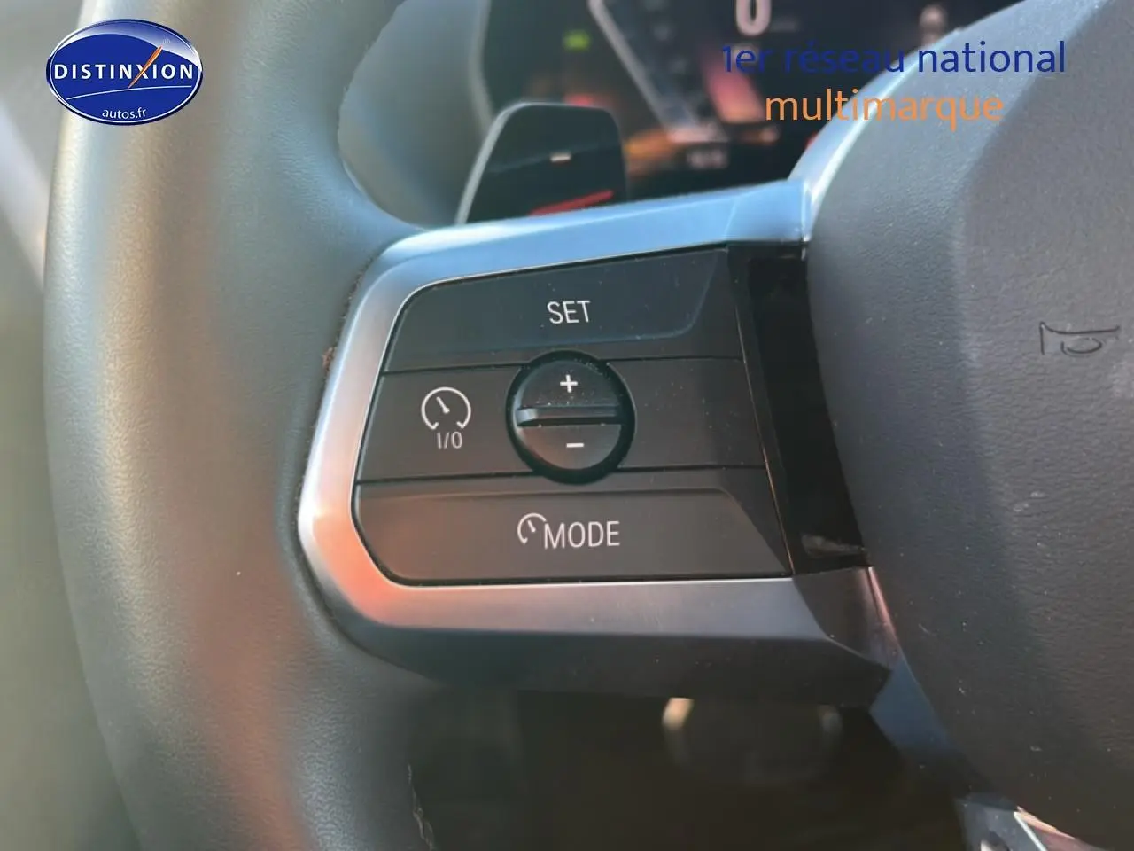 Gros plan sur les commandes du volant à gauche de la BMW Série 1 blanche, boutons de régulateur de vitesse et mode.