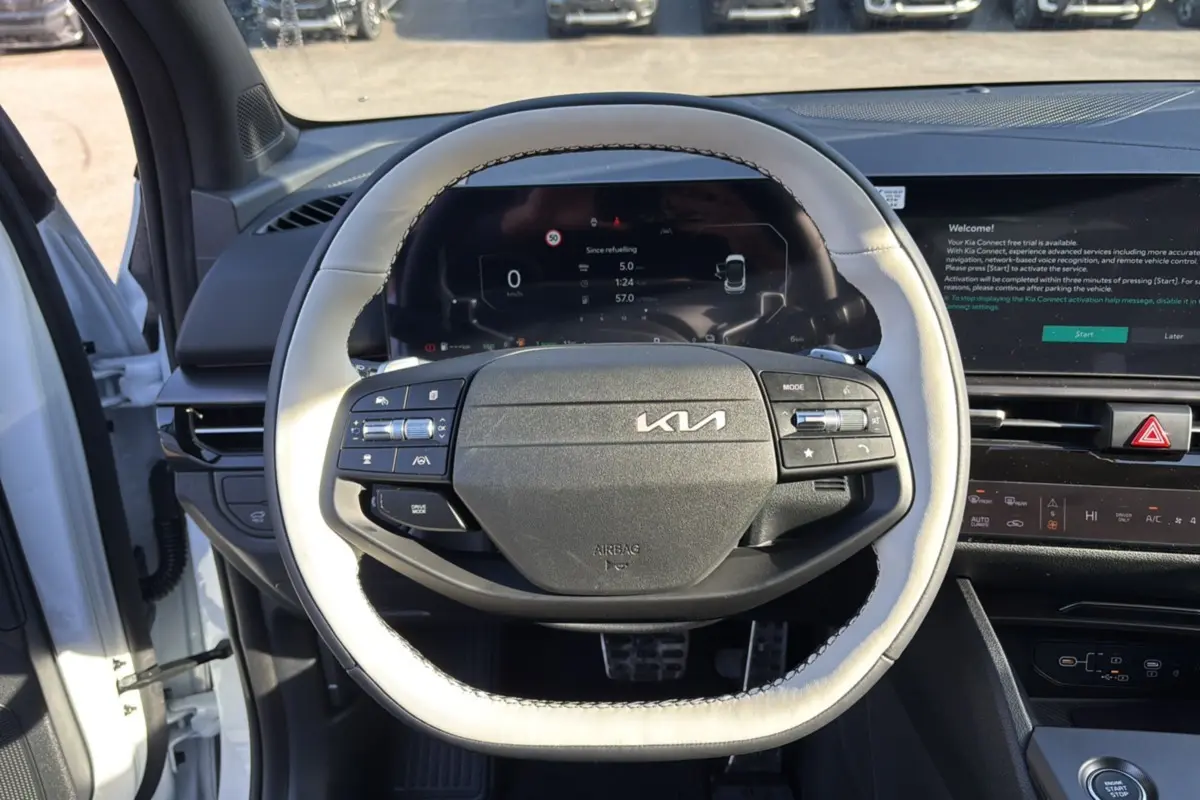 Vue intérieure centrée sur le volant cuir clair du Kia Sportage 2026 blanc nacré avec tableau de bord numérique.