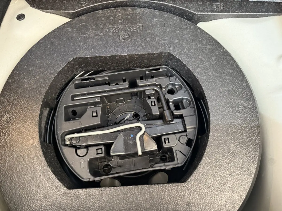Vue rapprochée de l'espace de rangement sous plancher dans le coffre d'une Citroën C3 blanche, montrant les outils de secours.