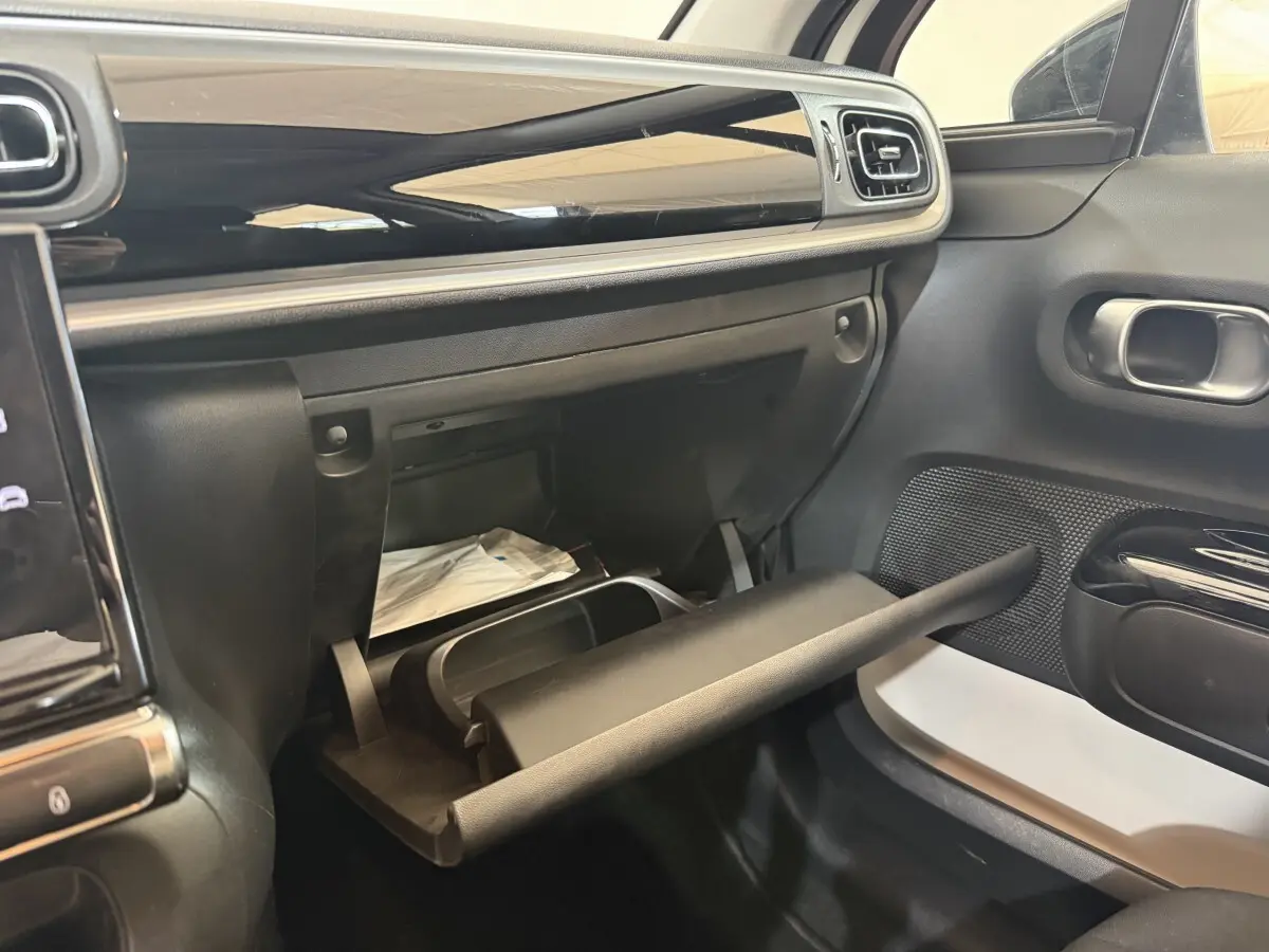 Vue intérieure côté passager de la Citroën C3 blanche 2021 avec boîte à gants ouverte et tableau de bord noir brillant.