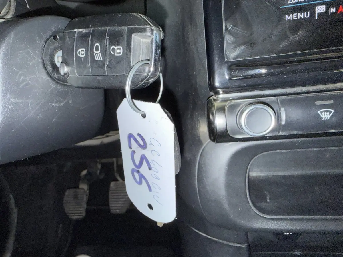 Gros plan sur la clé de contact avec étiquette suspendue dans l'habitacle noir d'une Citroën C3 blanche.