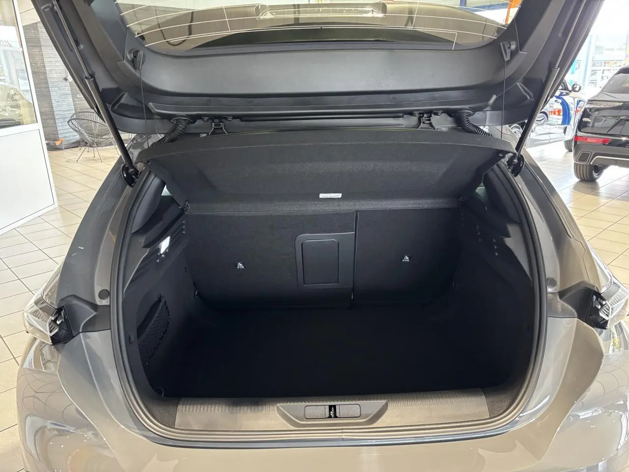 Coffre ouvert vu de l'arrière d'une Peugeot 308 gris selenium, montrant un espace de chargement vide et propre.