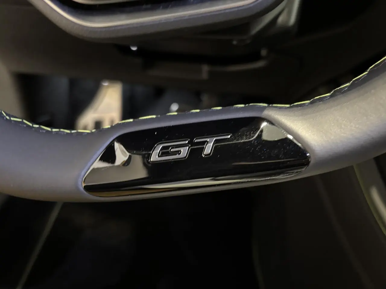 Gros plan sur le volant noir avec surpiqûres vert Adamite et logo GT brillant de la Peugeot 308 Hybrid 2026.
