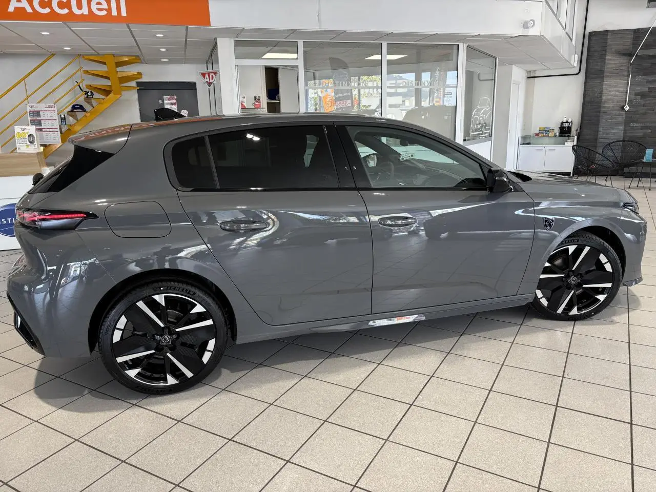 Peugeot 308 gris sélénium vue de profil côté gauche en intérieur avec jantes alliage bicolores et vitres teintées.