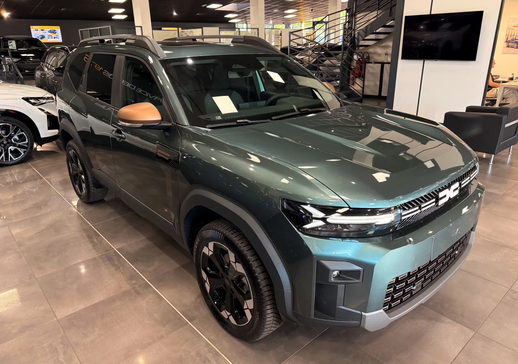 Vue 3/4 avant du Dacia Bigster Hybrid-G 150 4x4 en Vert Cèdre avec rétroviseurs bronze et jantes bi-ton noir.