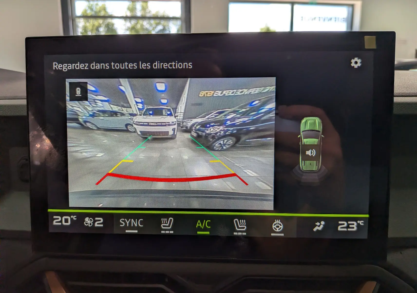 Vue caméra de recul montrant un Dacia Bigster Vert Cèdre de face dans un parking intérieur avec lignes de guidage colorées.