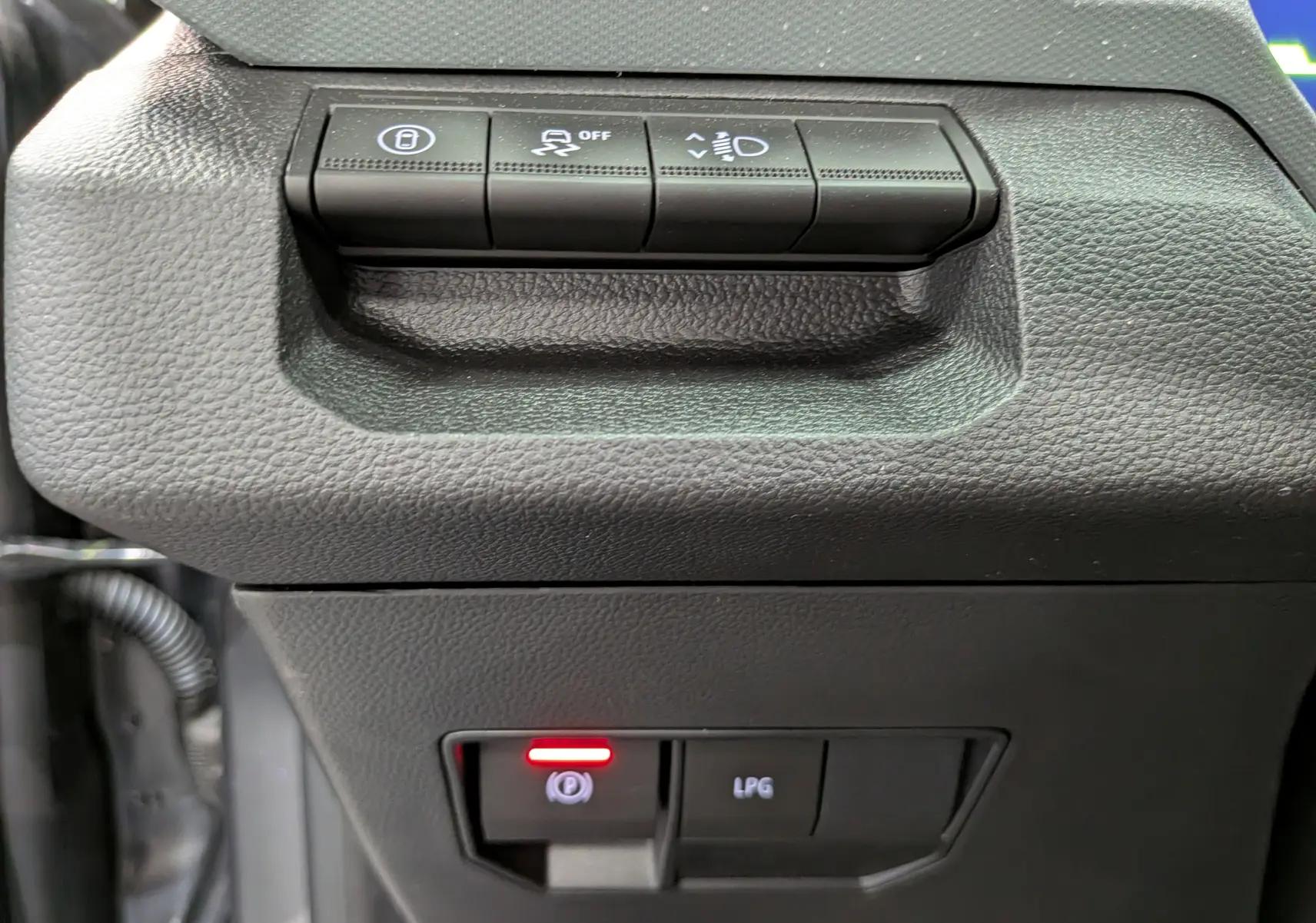 Gros plan sur les commandes de tableau de bord noir du Dacia Bigster Hybrid-G 150, avec bouton frein à main électronique allumé.