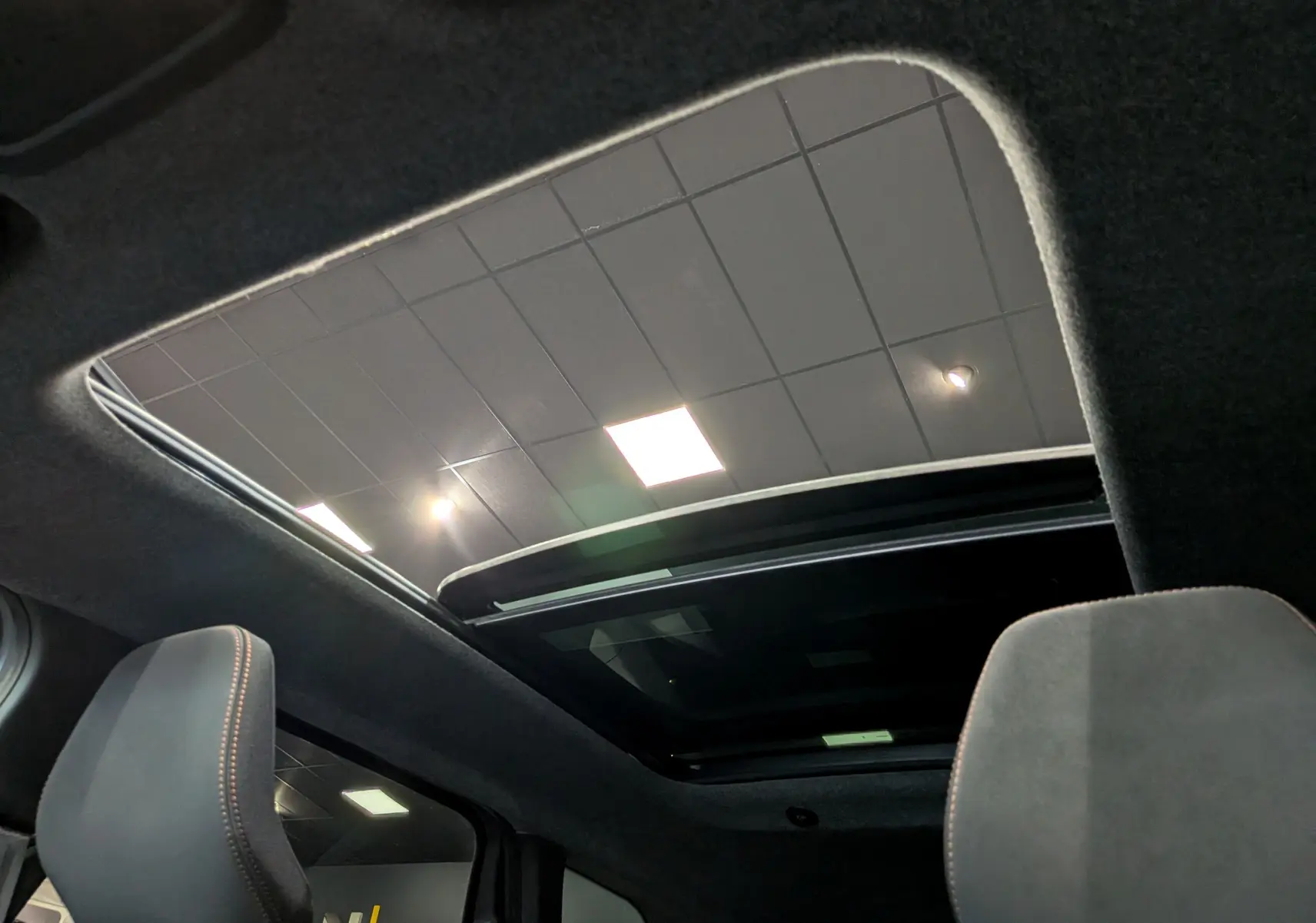 Toit ouvrant panoramique vu de l'intérieur du Dacia Bigster Hybrid-G 150 4x4, avec ciel de toit noir et sièges gris.